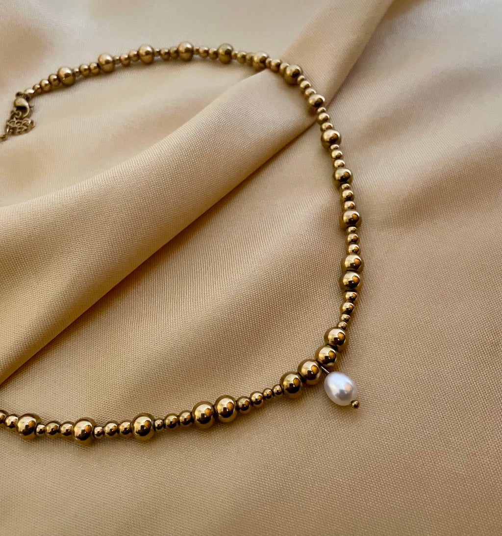 Close-up of a gold beaded choker necklace featuring a single white AAA grade oval pearl pendant