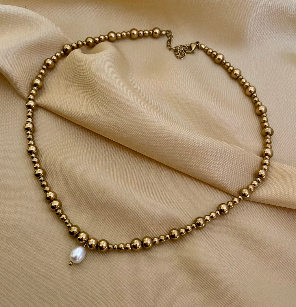 Close-up of a woman wearing a gold beaded choker necklace featuring a single white AAA grade oval pearl pendant, styled with a beige open silk shirt