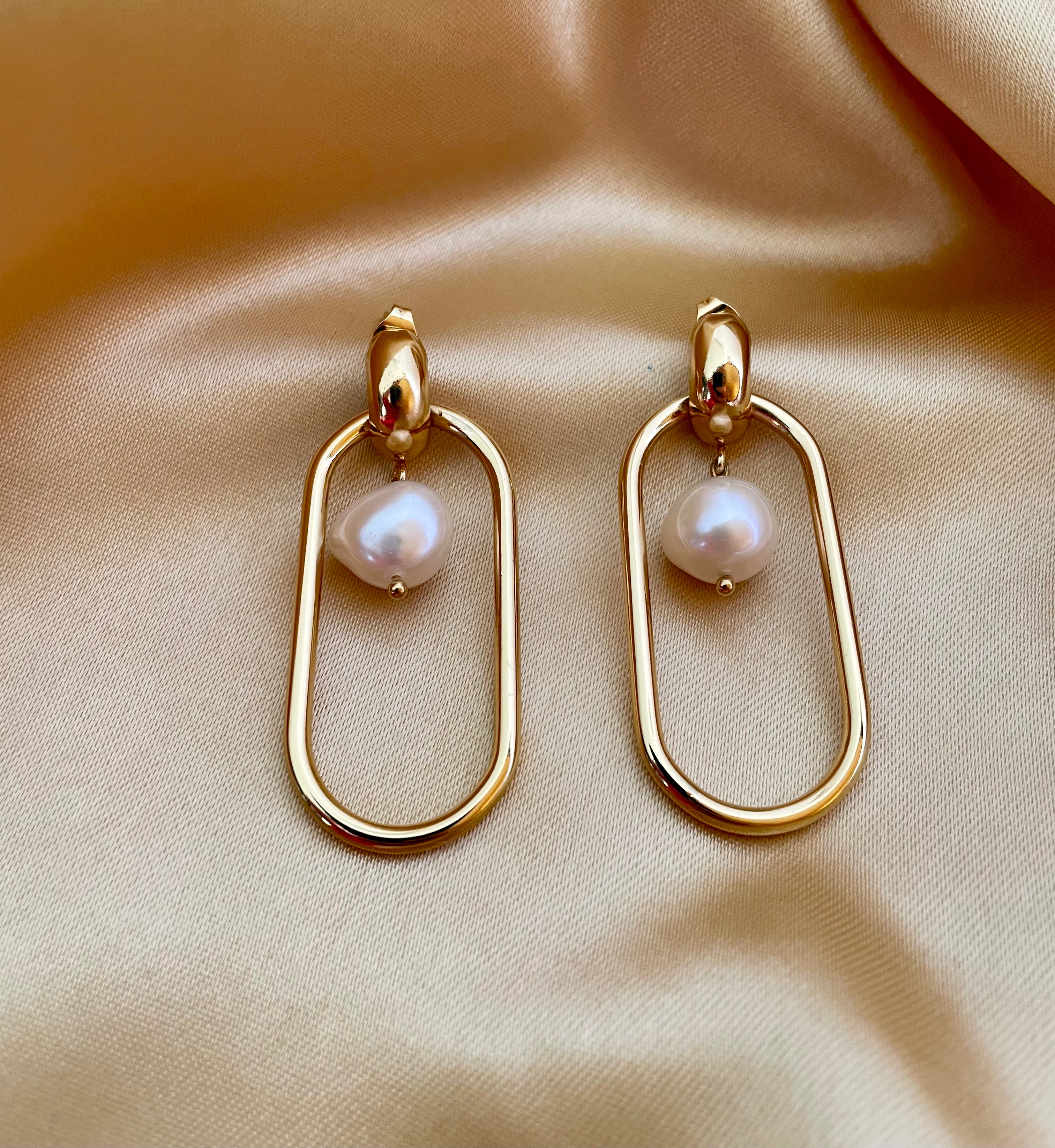 Editorial shot of a model wearing modern geometric gold hoop earrings with a floating freshwater pearl center, set against a warm ivory background