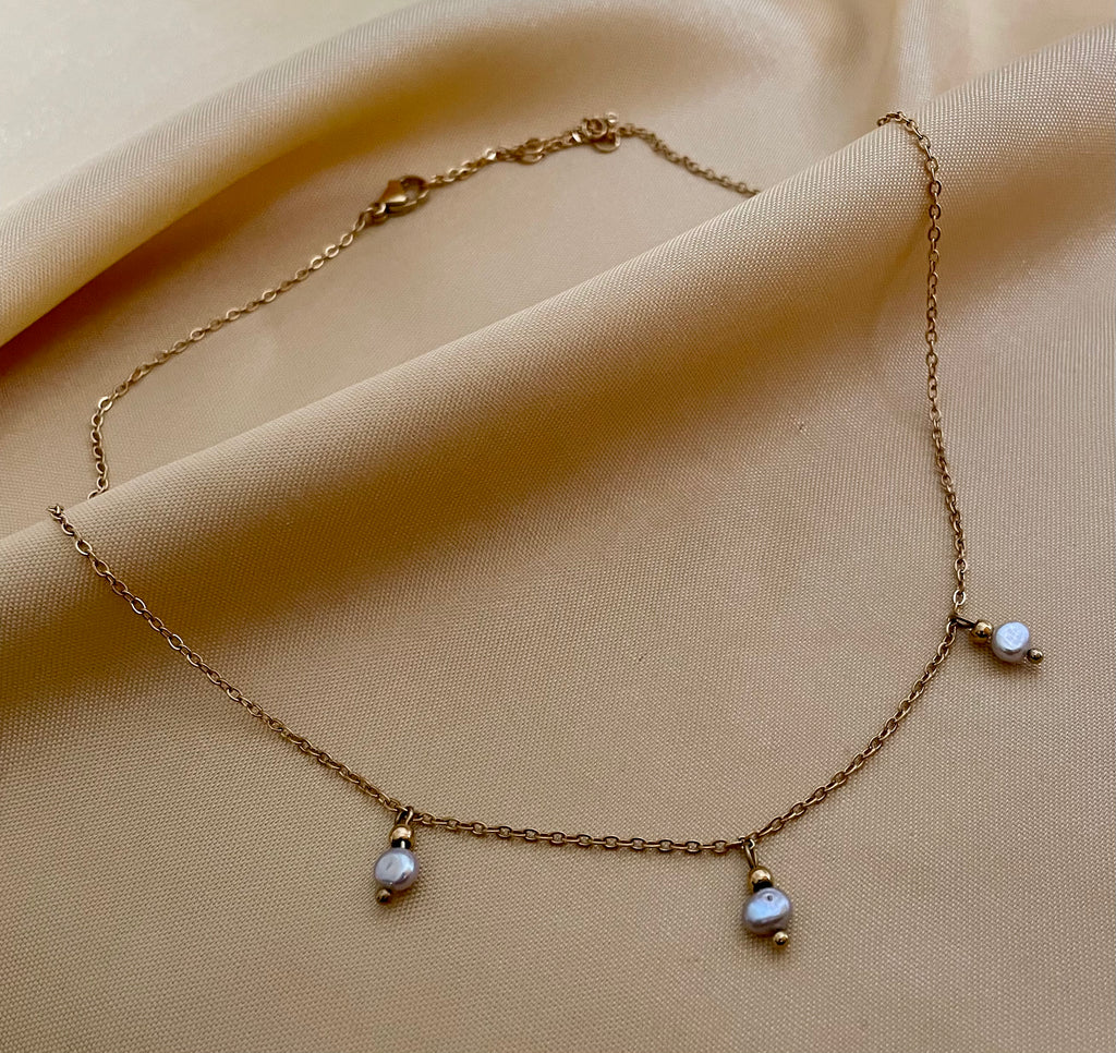 Close-up detail of a delicate gold chain necklace featuring three small metallic grey baroque pearls with high luster. High-resolution jewelry photography highlighting the pearl texture and dainty chain links