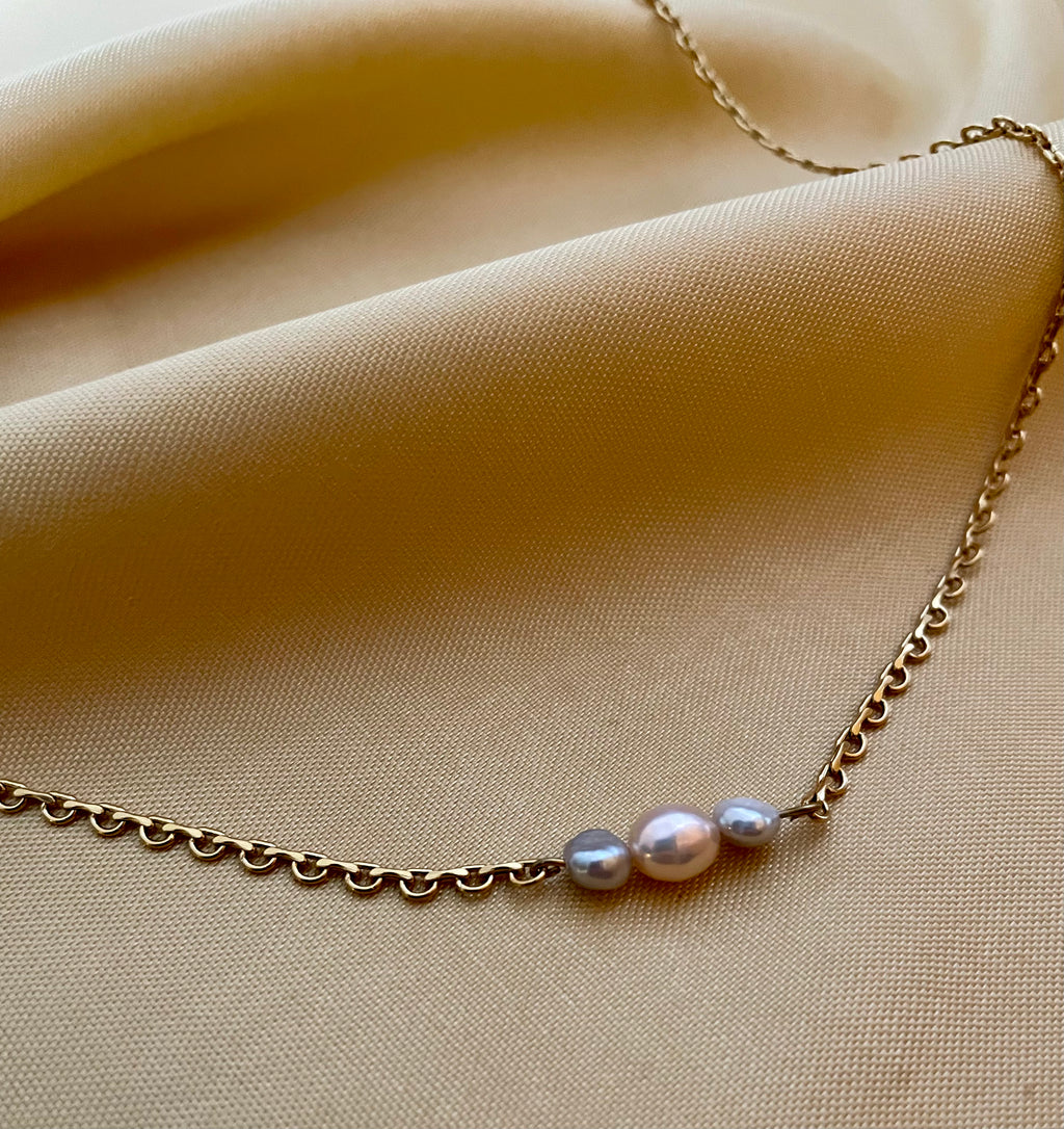 Delicate gold link chain necklace featuring a trio of pearls: a central oval pink pearl flanked by two smaller, irregular grey baroque pearls