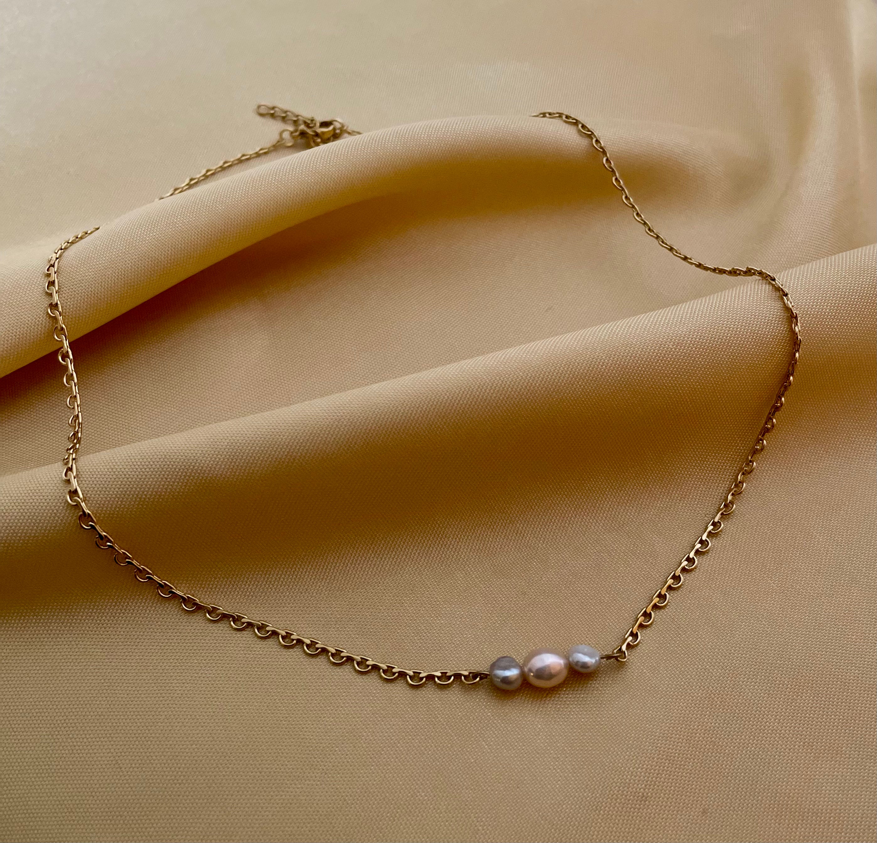 Delicate gold link chain necklace featuring a trio of pearls: a central oval pink pearl flanked by two smaller, irregular grey baroque pearls