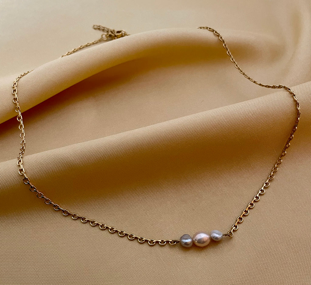Delicate gold link chain necklace featuring a trio of pearls: a central oval champagne pearl flanked by two smaller, irregular grey baroque pearls