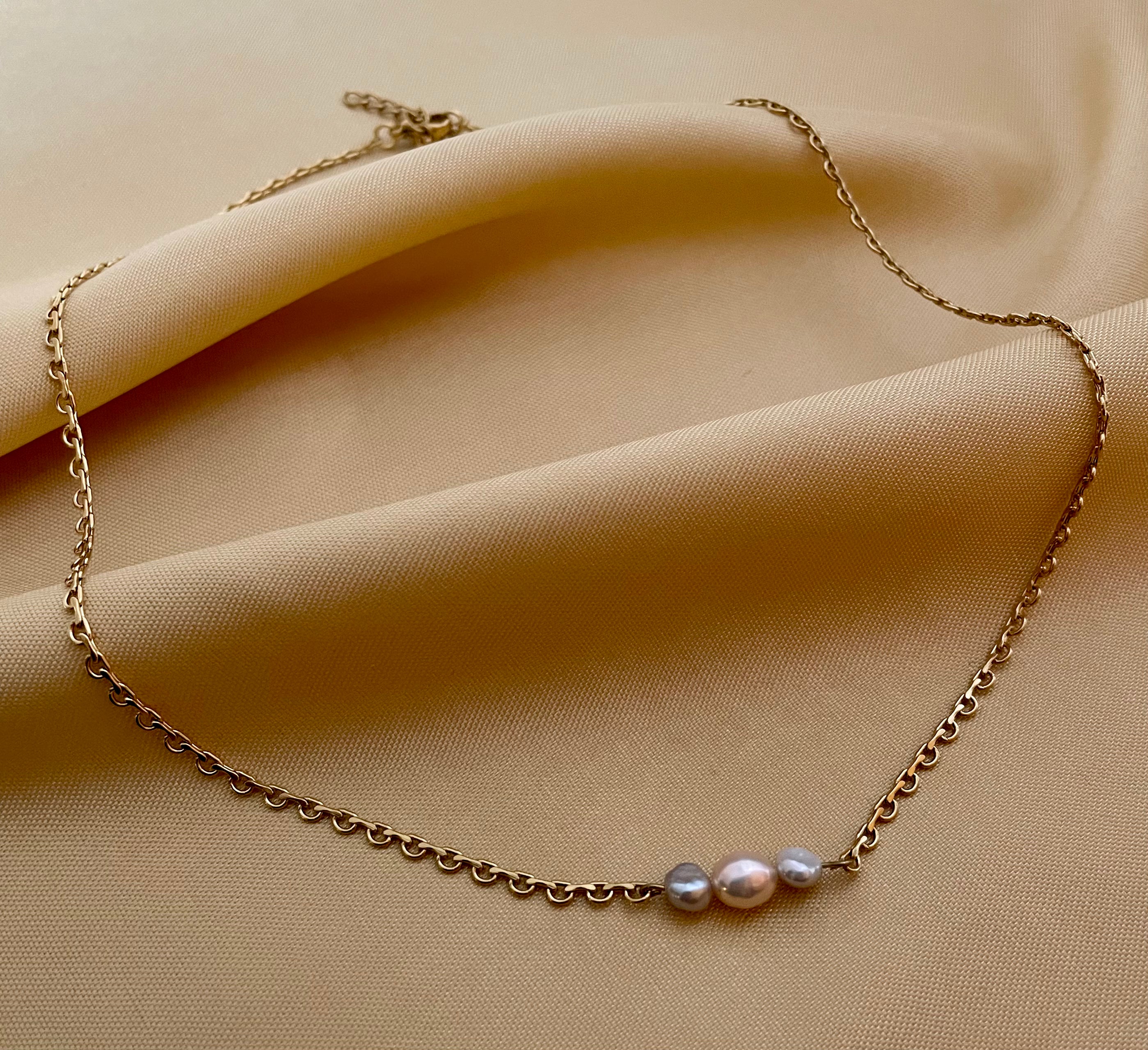 Delicate gold link chain necklace featuring a trio of pearls: a central oval champagne pearl flanked by two smaller, irregular grey baroque pearls