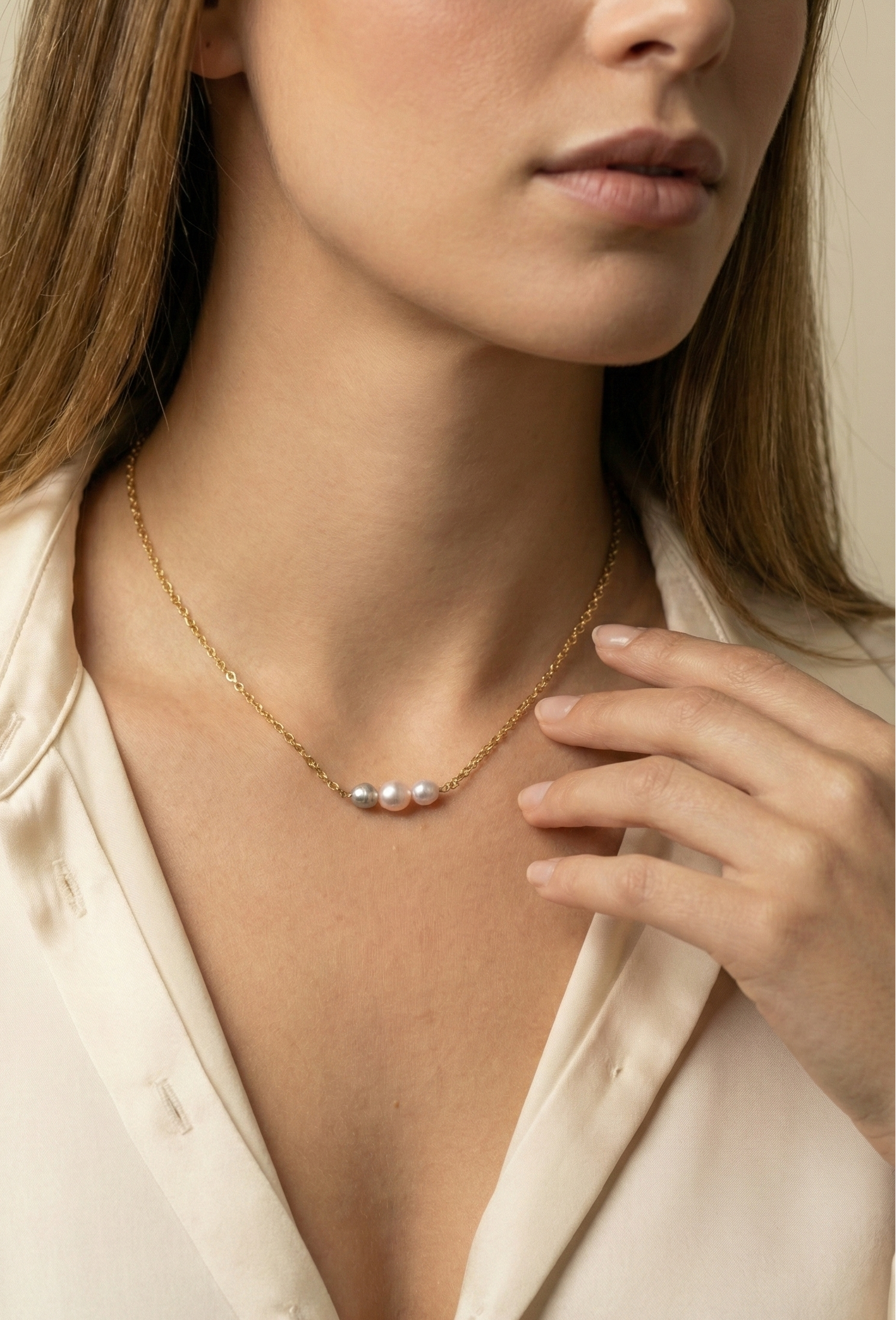Delicate gold link chain necklace featuring a trio of pearls: a central oval pink pearl flanked by two smaller, irregular grey baroque pearls
