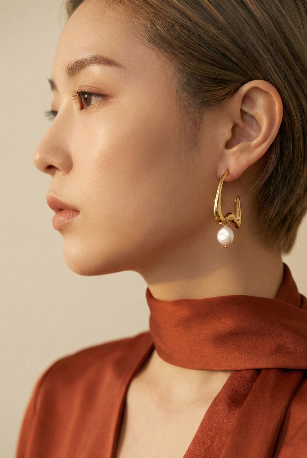 Woman wearing gold hoop earrings with a pearl against a neutral background