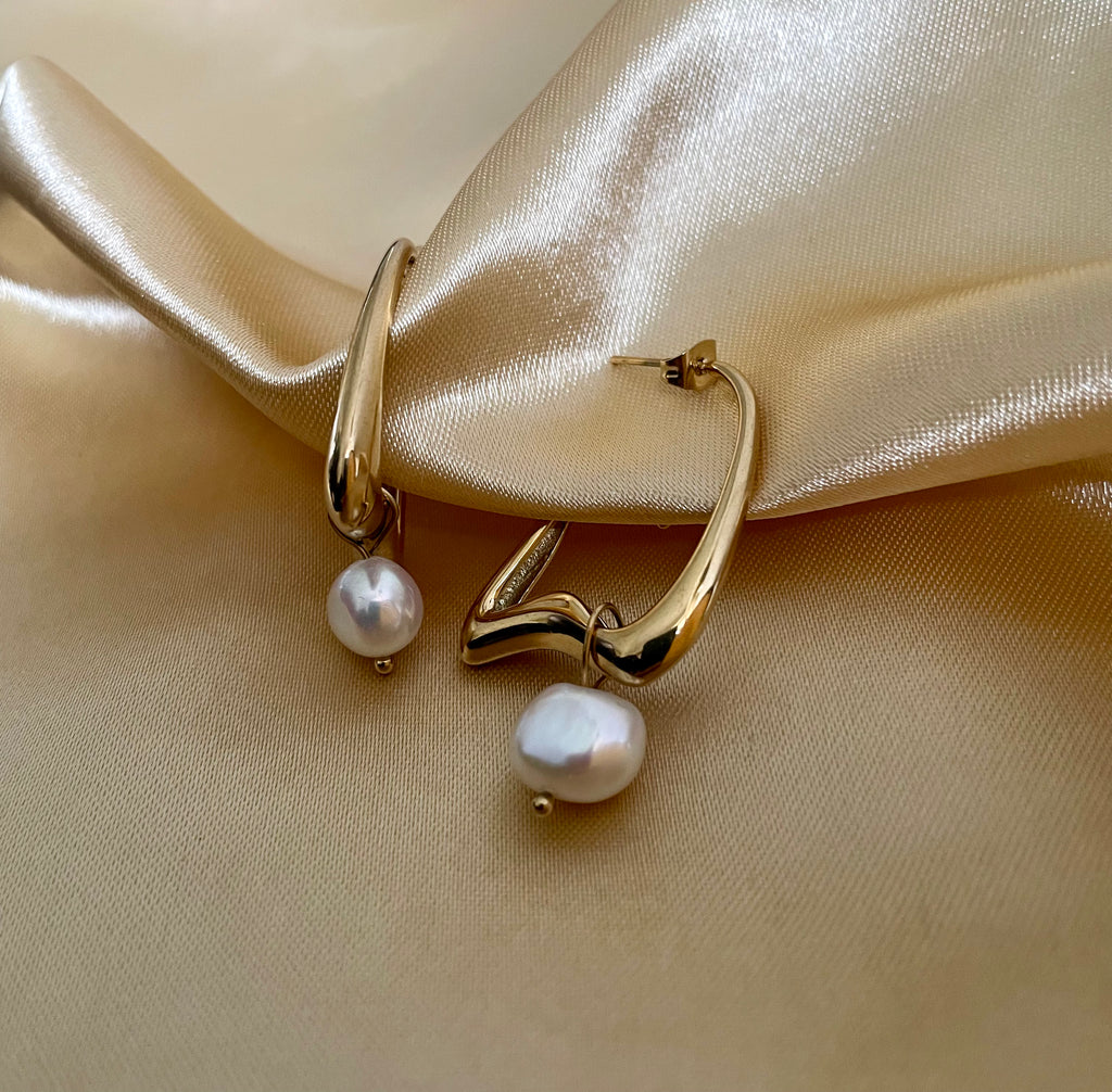 Gold hoop earrings with pearl drops on a beige fabric background