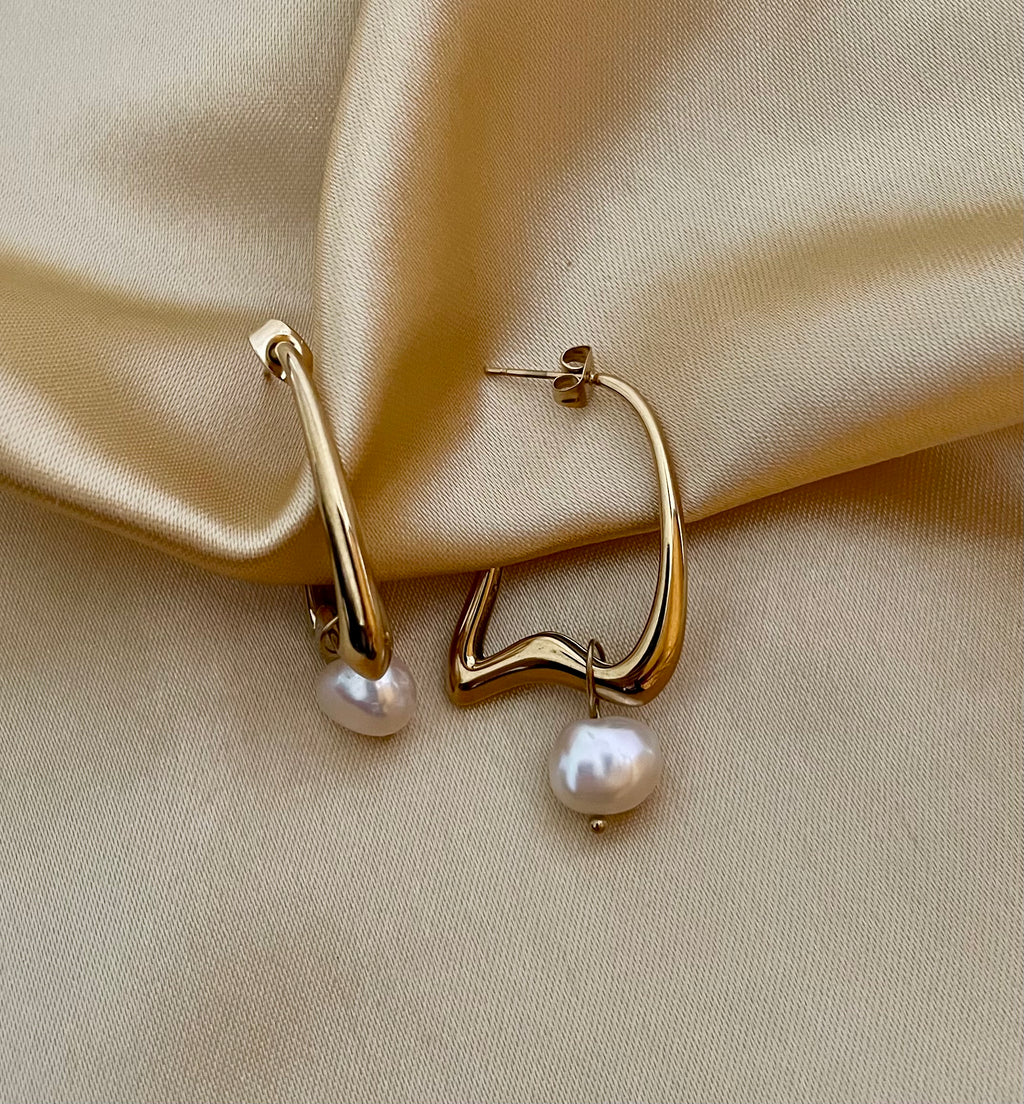 Gold hoop earrings with pearls on a beige satin background