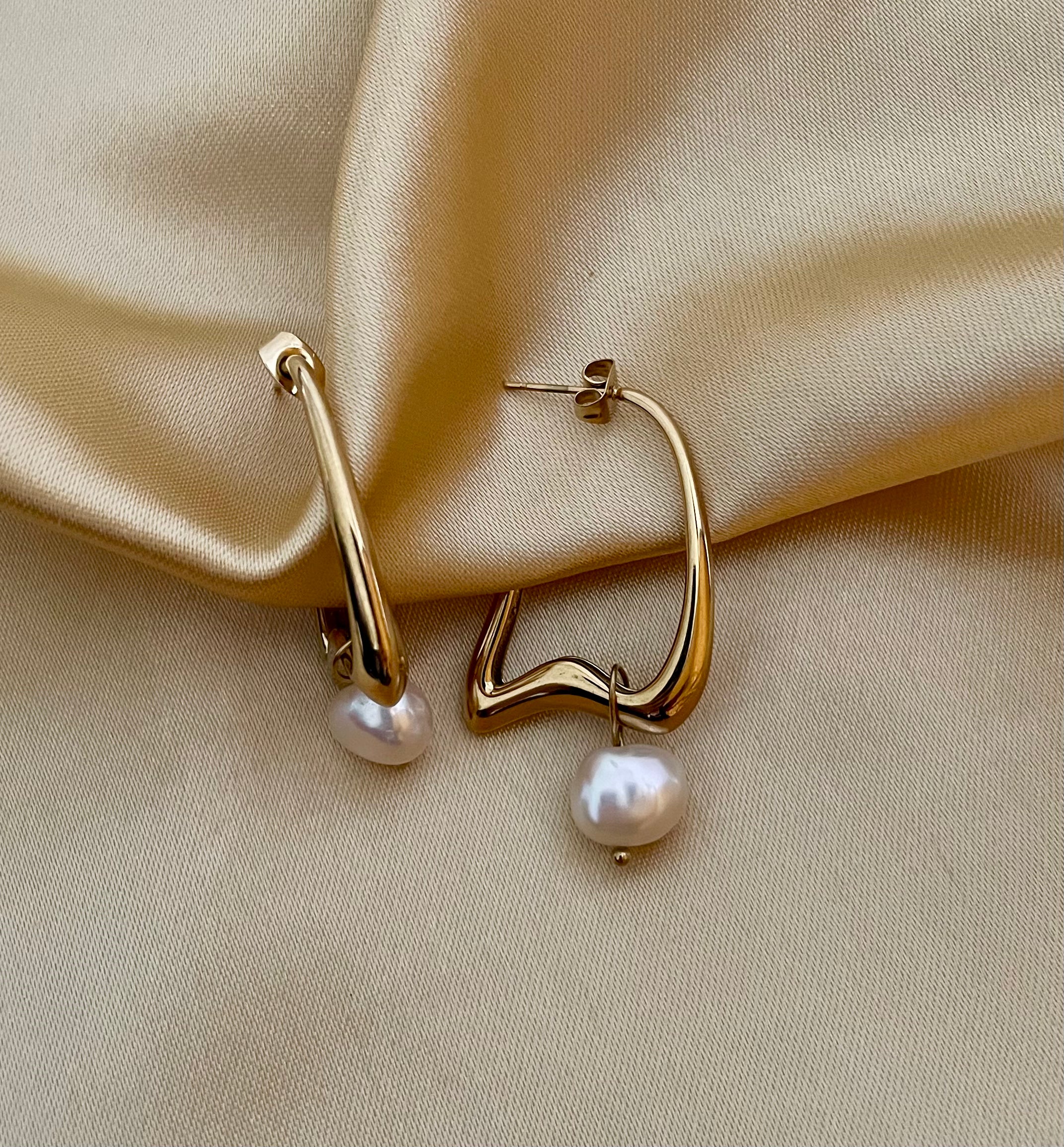 Gold hoop earrings with pearls on a beige satin background