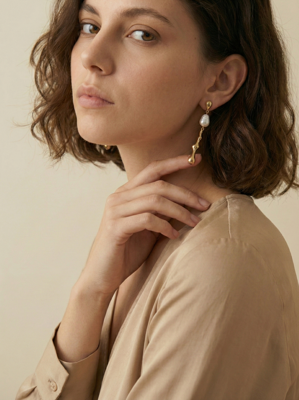Woman wearing keshi gold earrings with a beige background