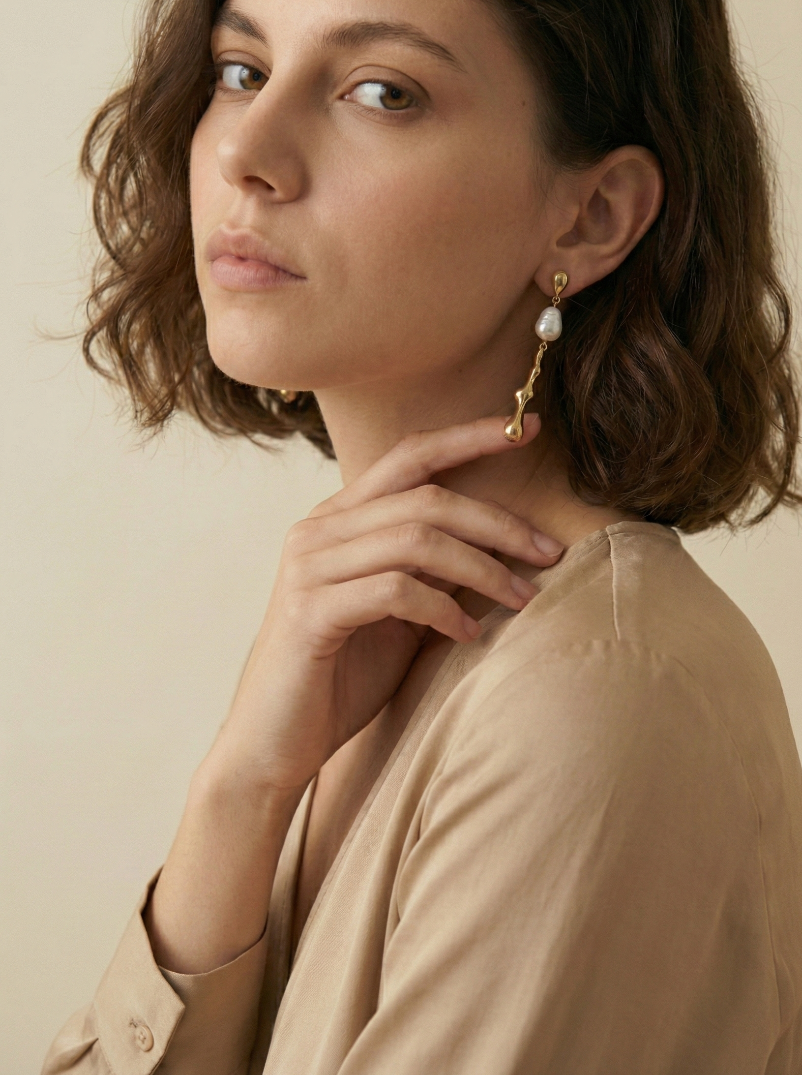 Woman wearing keshi gold earrings with a beige background
