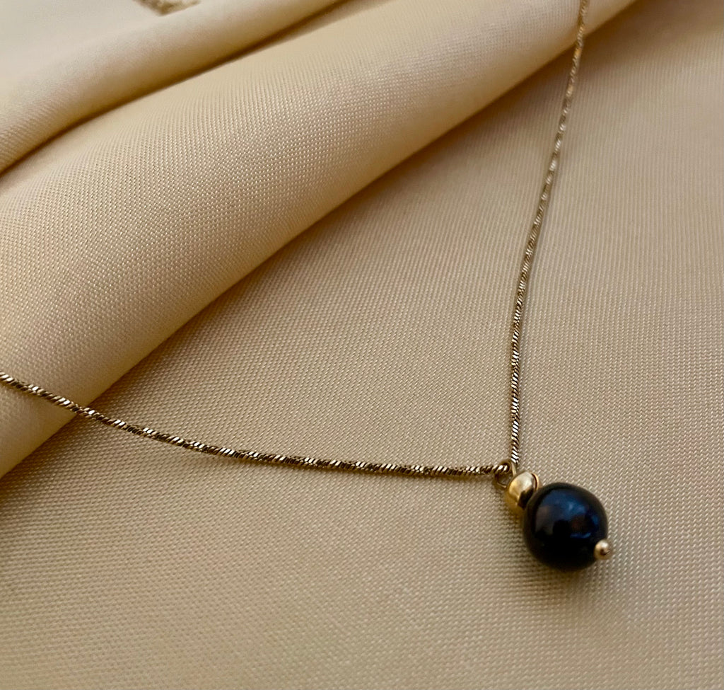 Elegant black pearl solitaire necklace on a twisted gold chain. Luxury jewelry editorial photography 