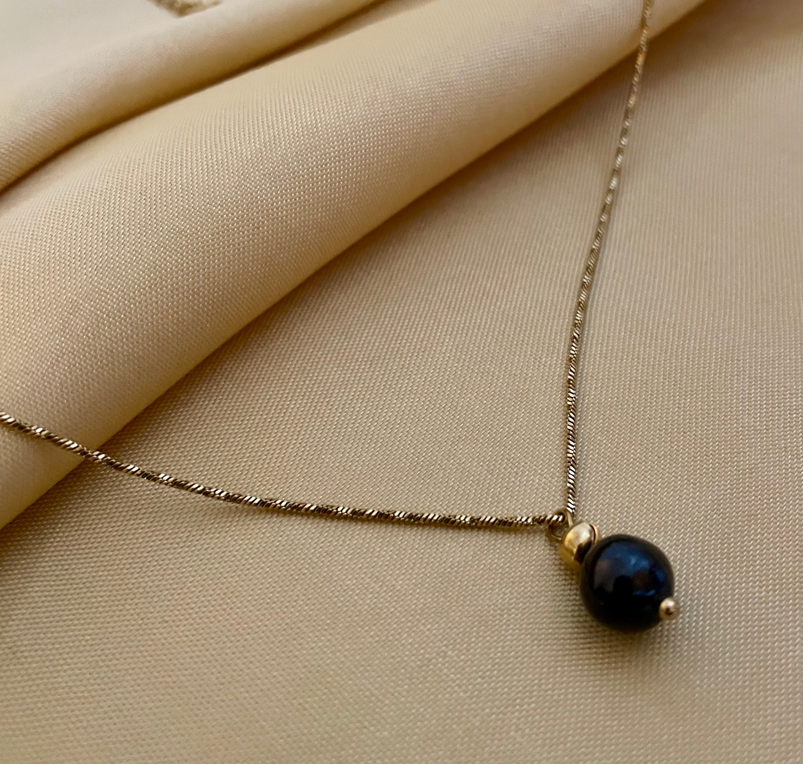 Elegant black pearl solitaire necklace on a twisted gold chain. Luxury jewelry editorial photography 