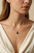 Elegant black pearl solitaire necklace on a twisted gold chain. Luxury jewelry editorial photography featuring a woman in a cream silk blouse with soft studio lighting.