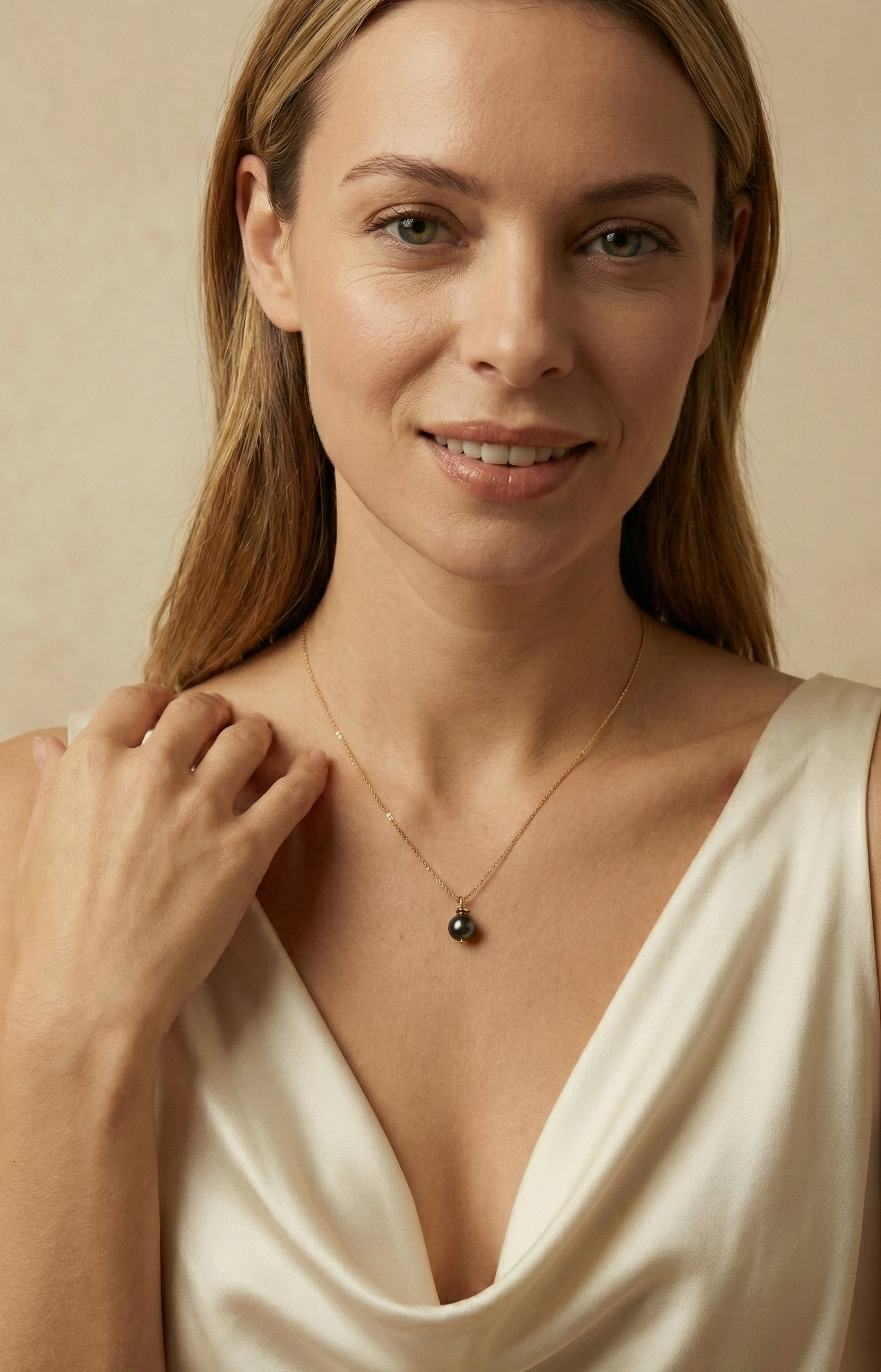 Elegant black pearl solitaire necklace on a twisted gold chain. Luxury jewelry editorial photography featuring a woman in a cream silk blouse with soft studio lighting.
