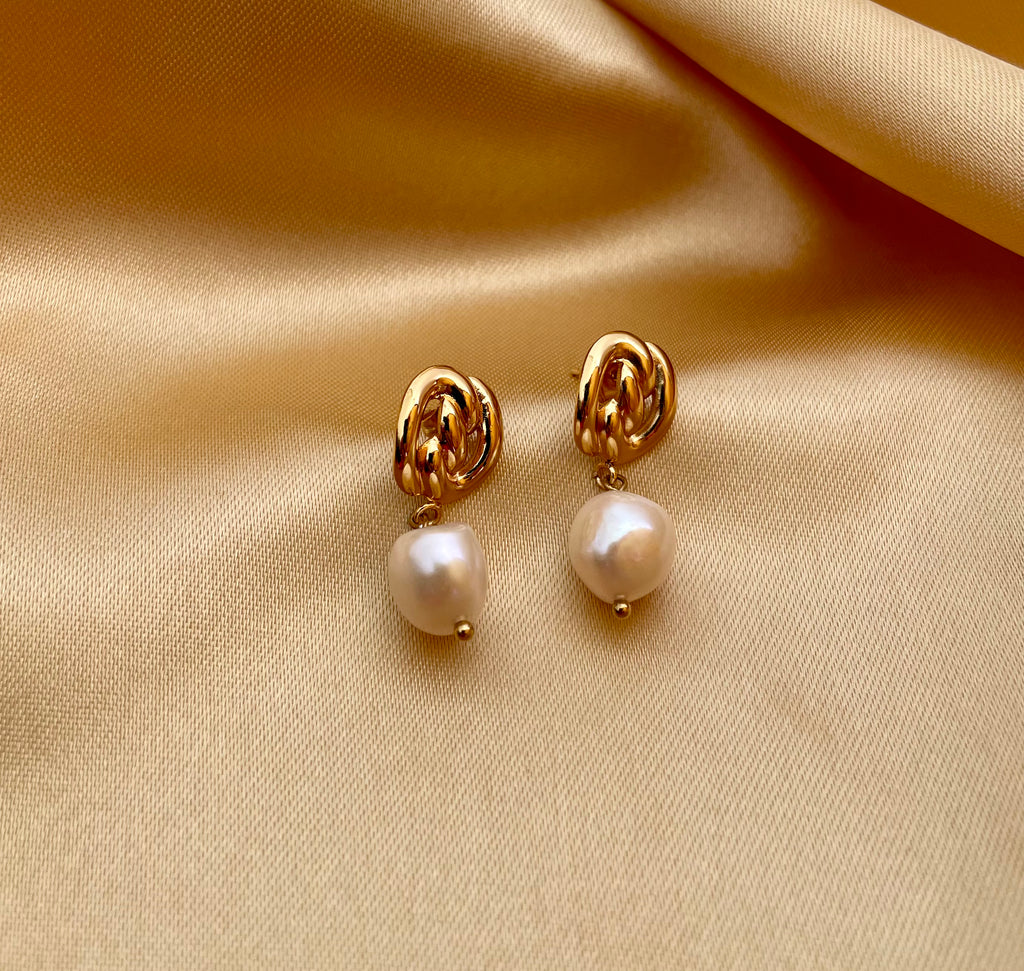 Gold pearl drop earrings featuring a chunky gold knot design and genuine white pearls. Modeled on an ear to show scale and fit