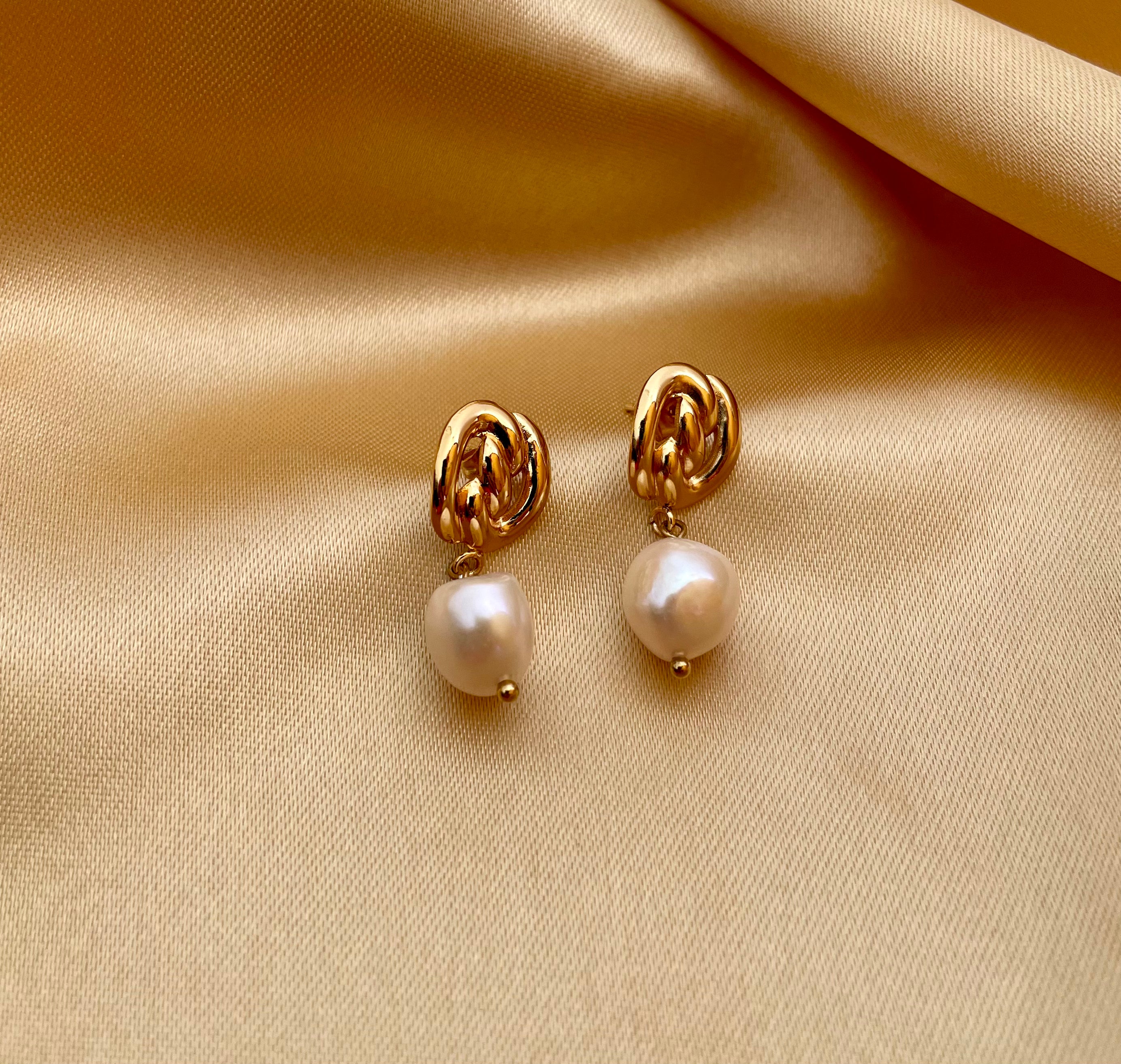 Gold pearl drop earrings featuring a chunky gold knot design and genuine white pearls. Modeled on an ear to show scale and fit