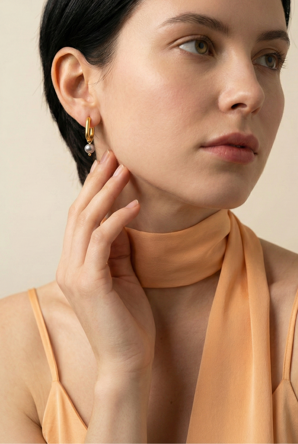 Woman wearing minimalist yellow gold hoop earrings with a small, organic grey pearl dangle.