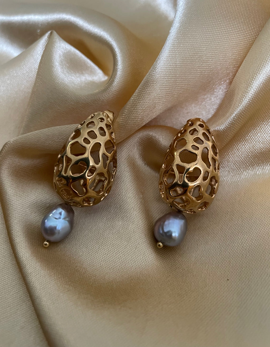 Elegant side-profile of a blonde model wearing sophisticated gold and grey pearl drop earrings paired with an unbuttoned ivory blouse.