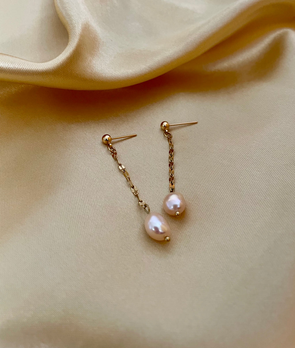 Pair of pearl earrings on a beige fabric background