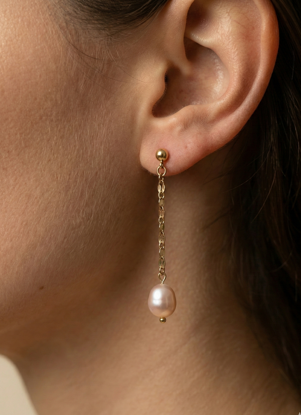 Close-up of an ear wearing a gold earring with a pearl drop.