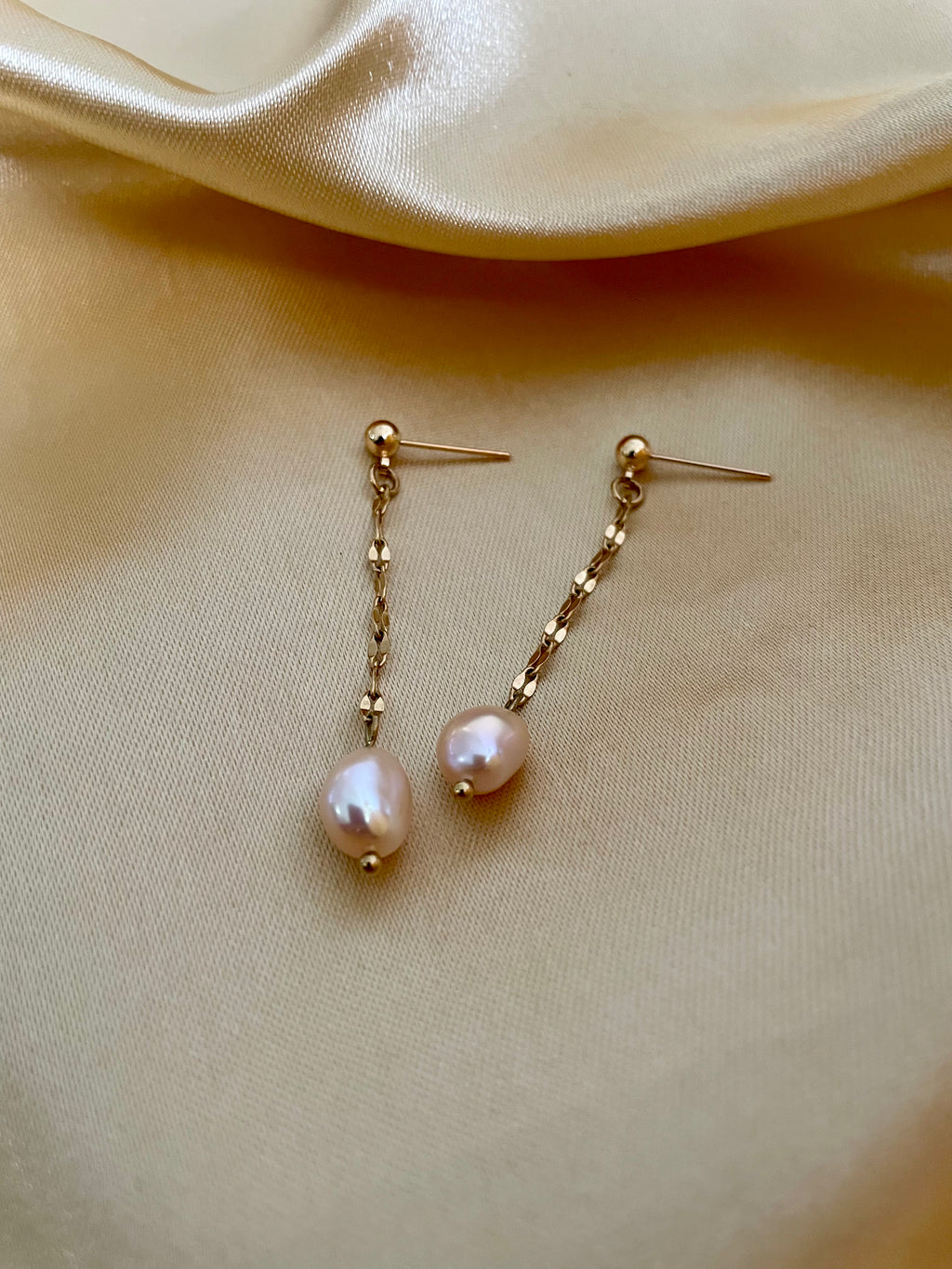 Pair of pearl earrings on a beige fabric background