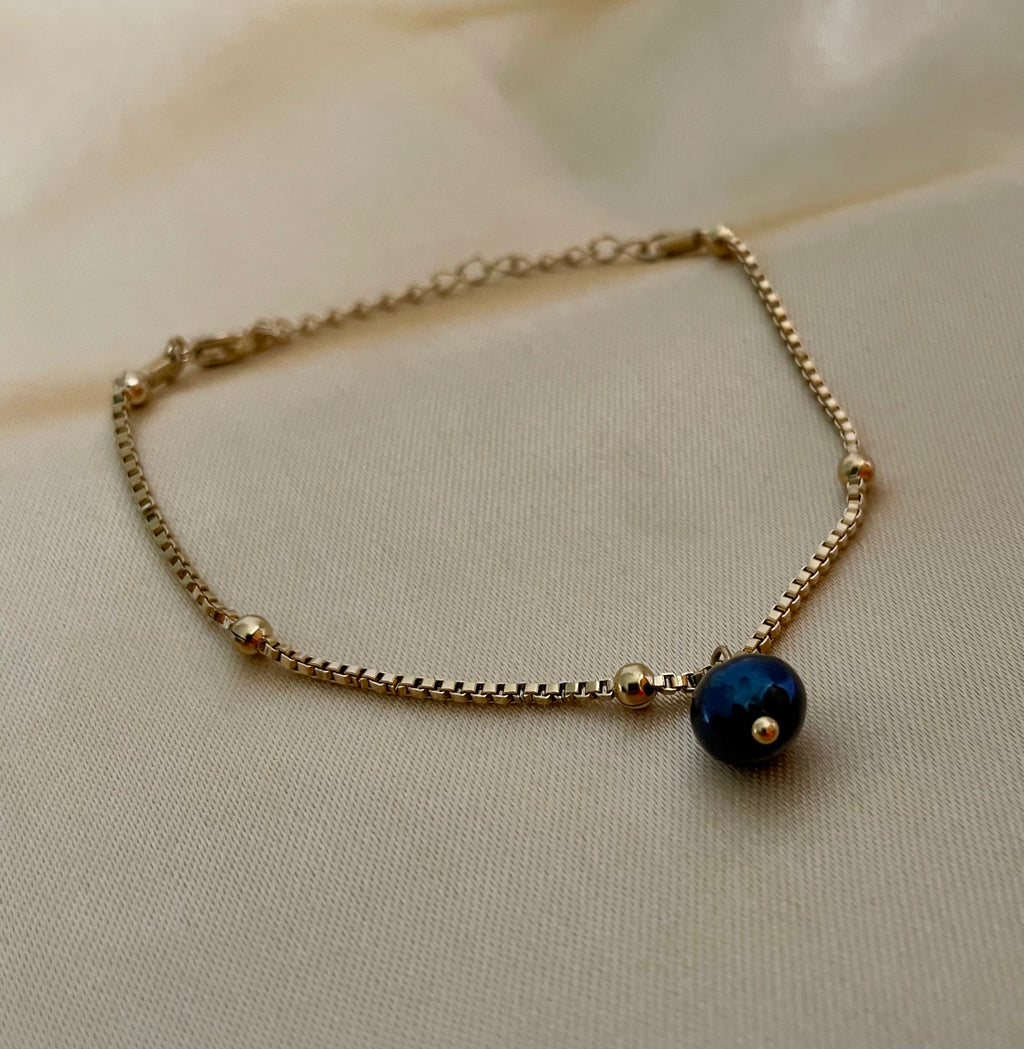 Gold bracelet with a blue bead on a beige fabric background