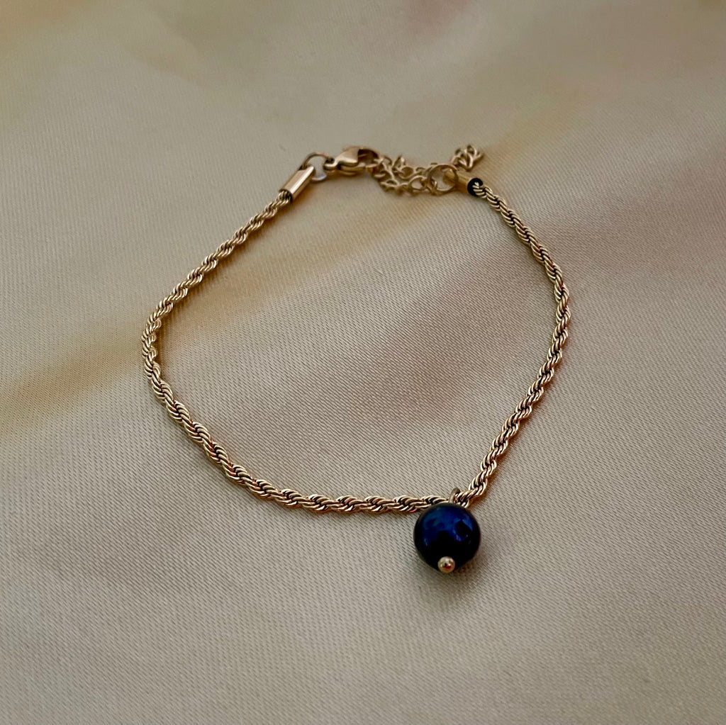Gold bracelet with a black pearl on a beige fabric background