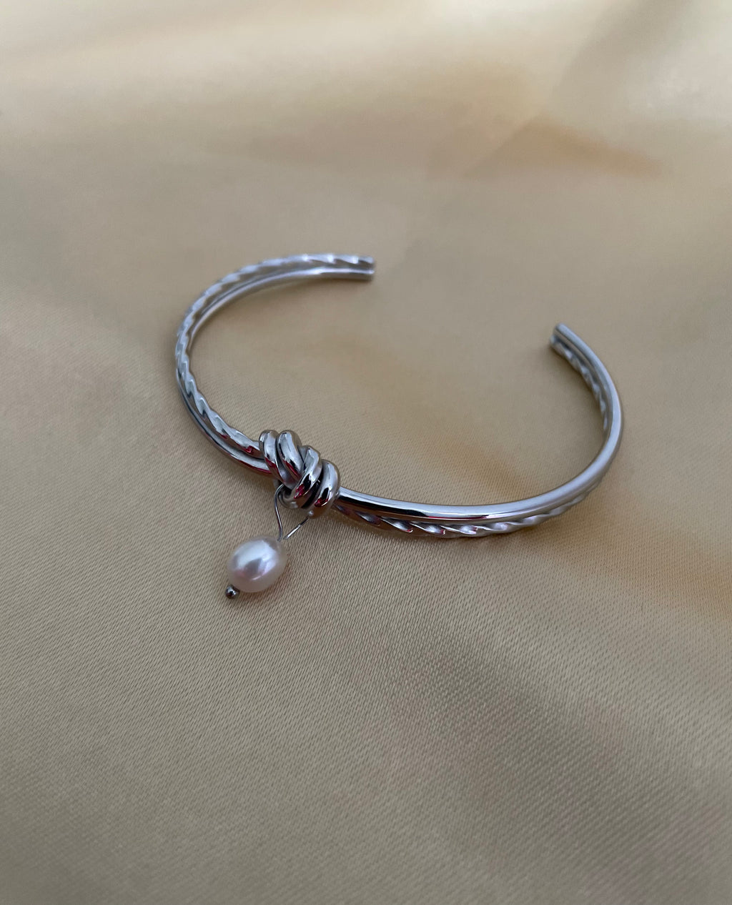 Silver bracelet with a pearl charm on a beige fabric background