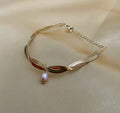Gold bracelet with a pearl pendant on a beige fabric background
