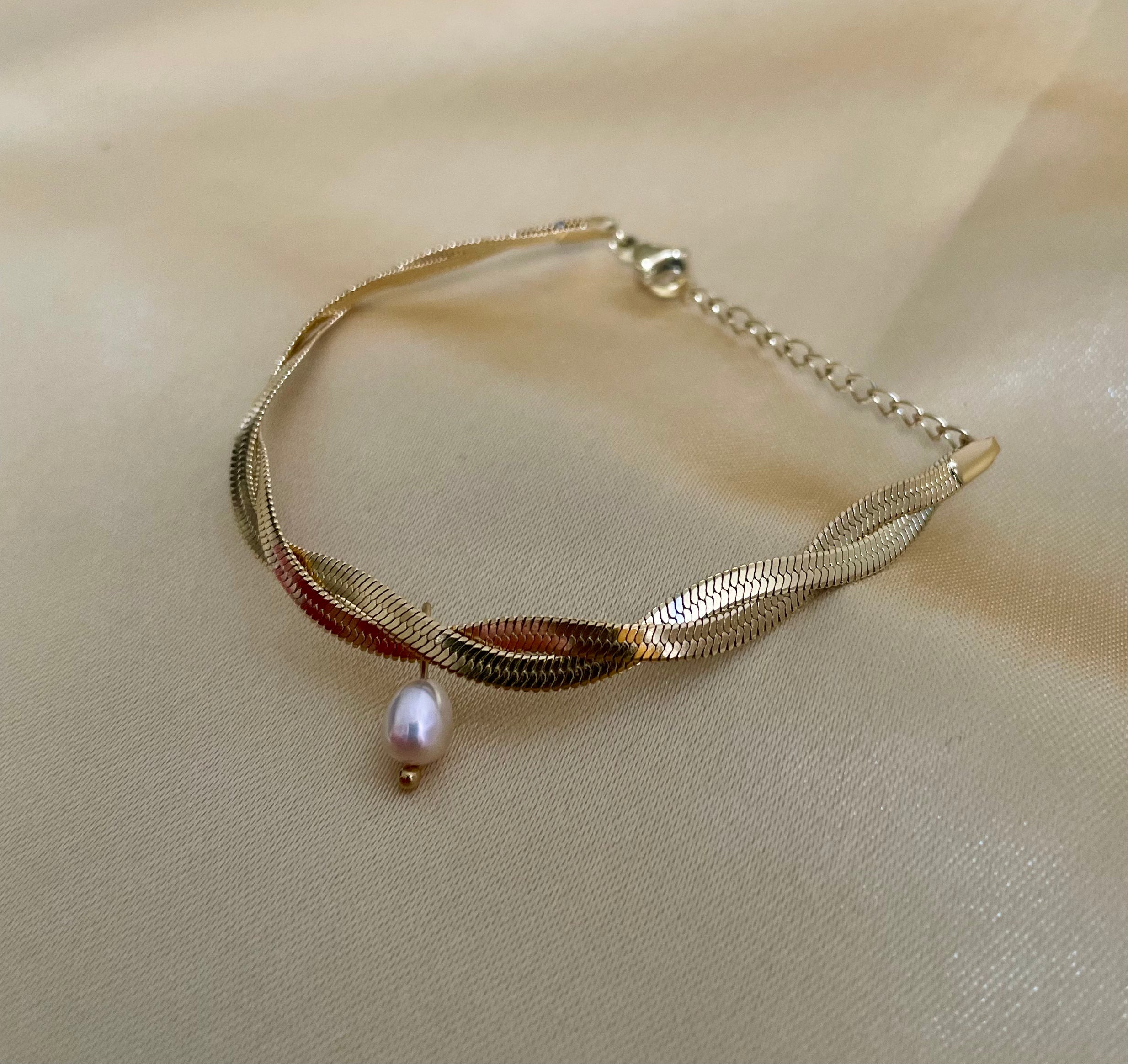 Gold bracelet with a pearl pendant on a beige fabric background