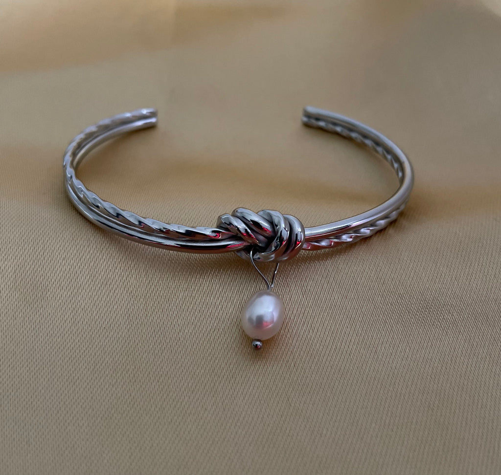 Silver bracelet with a pearl charm on a beige background