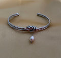 Silver bracelet with a pearl charm on a beige background