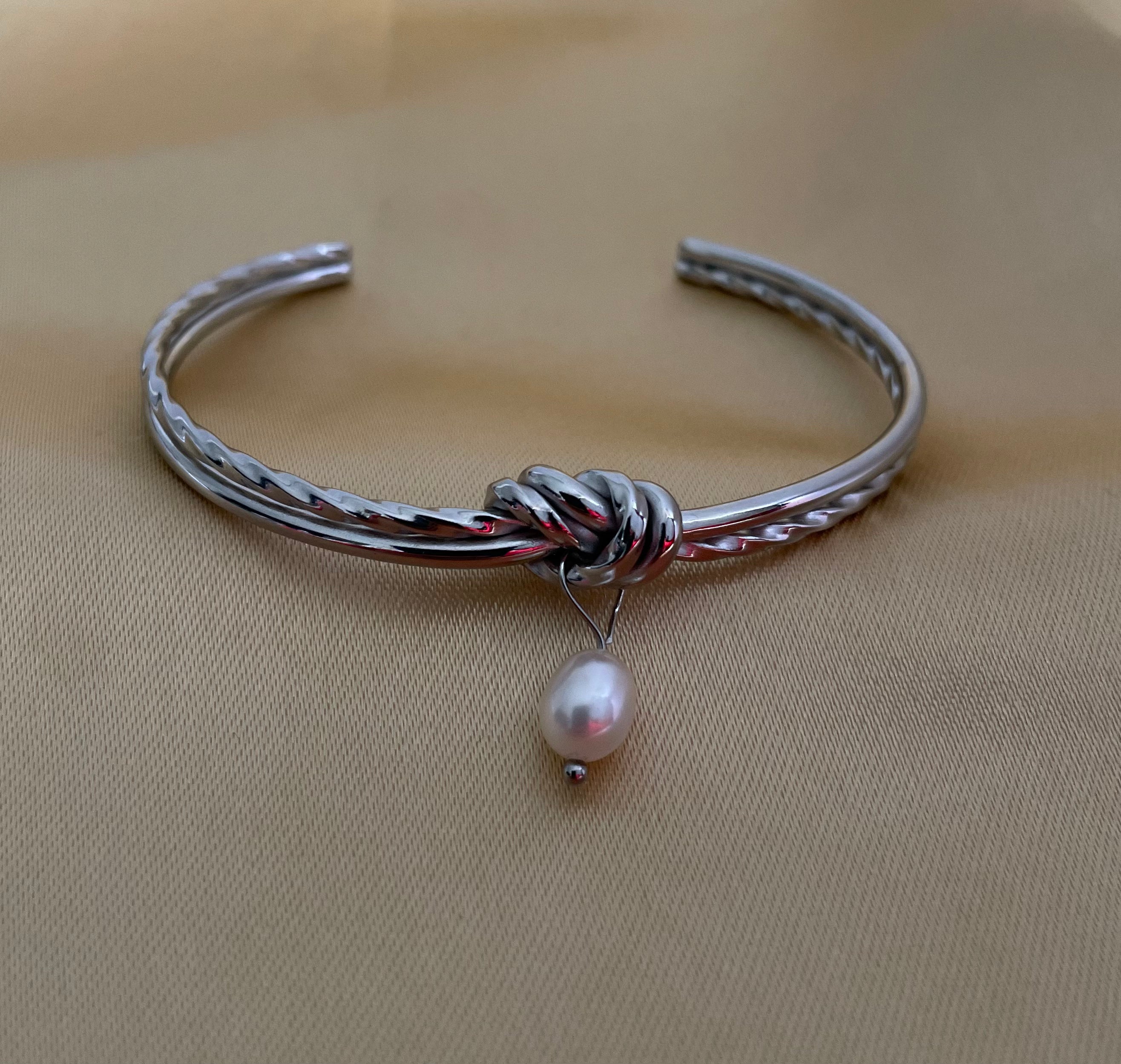 Silver bracelet with a pearl charm on a beige background