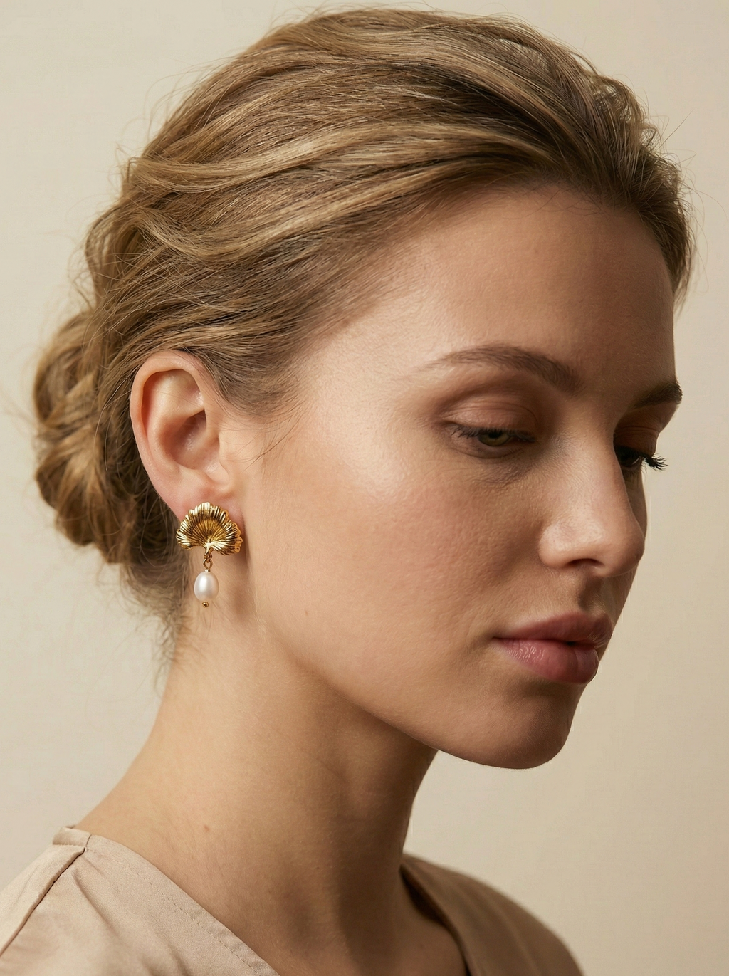 The earrings feature a detailed, textured gold fan shape resembling a ginkgo biloba leaf, from which hangs a lustrous white freshwater pearl.