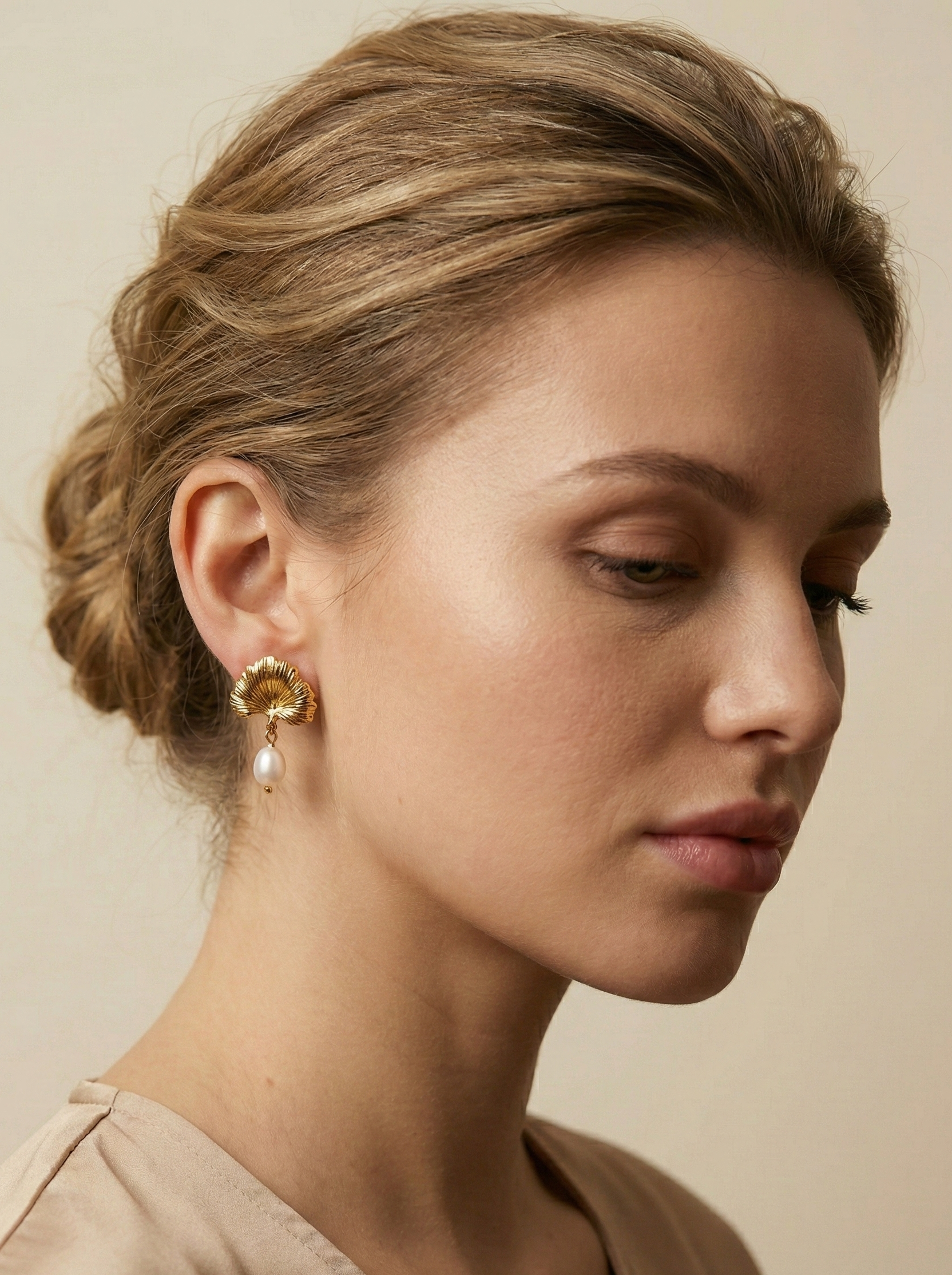 The earrings feature a detailed, textured gold fan shape resembling a ginkgo biloba leaf, from which hangs a lustrous white freshwater pearl.