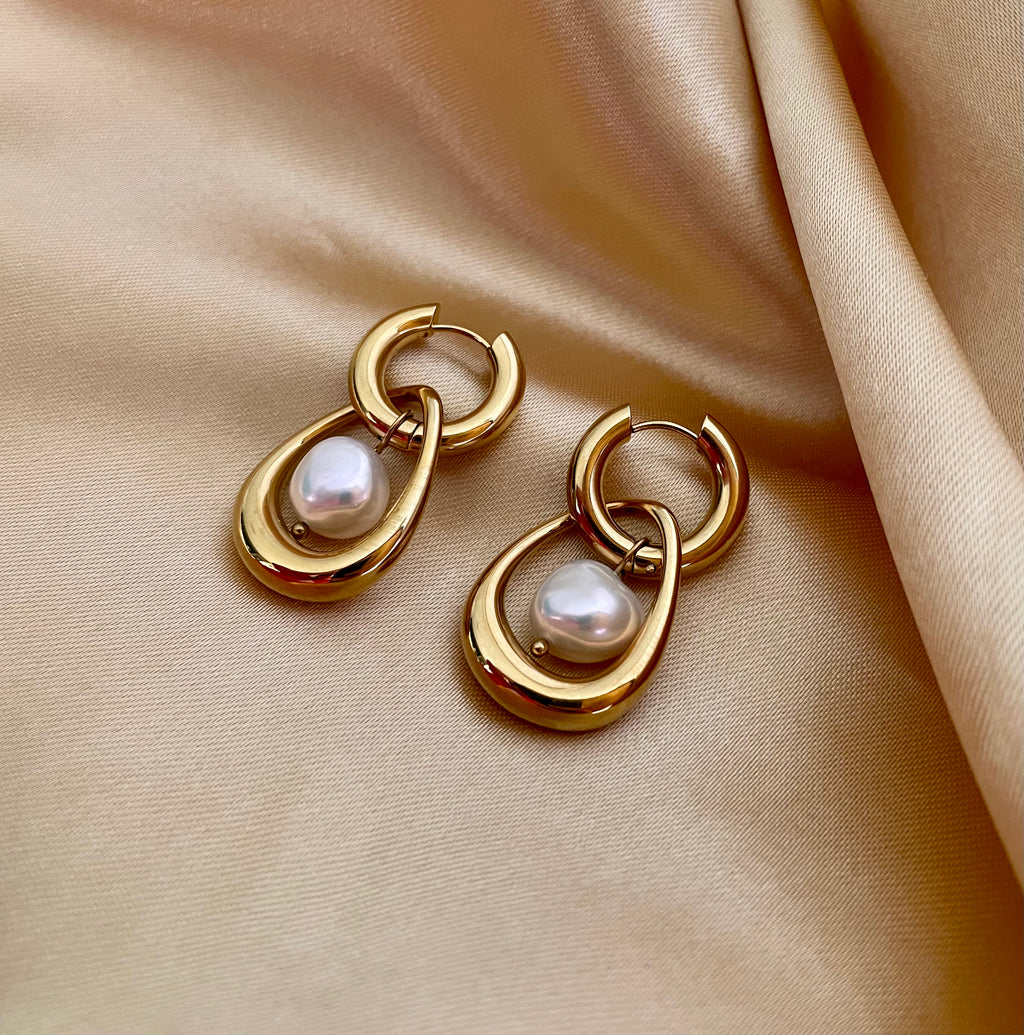 Close-up editorial photography of a gold hoop drop earring featuring a suspended organic white high-luster pearl. High-resolution luxury jewelry shot highlighting realistic gold texture and pearl iridescence.