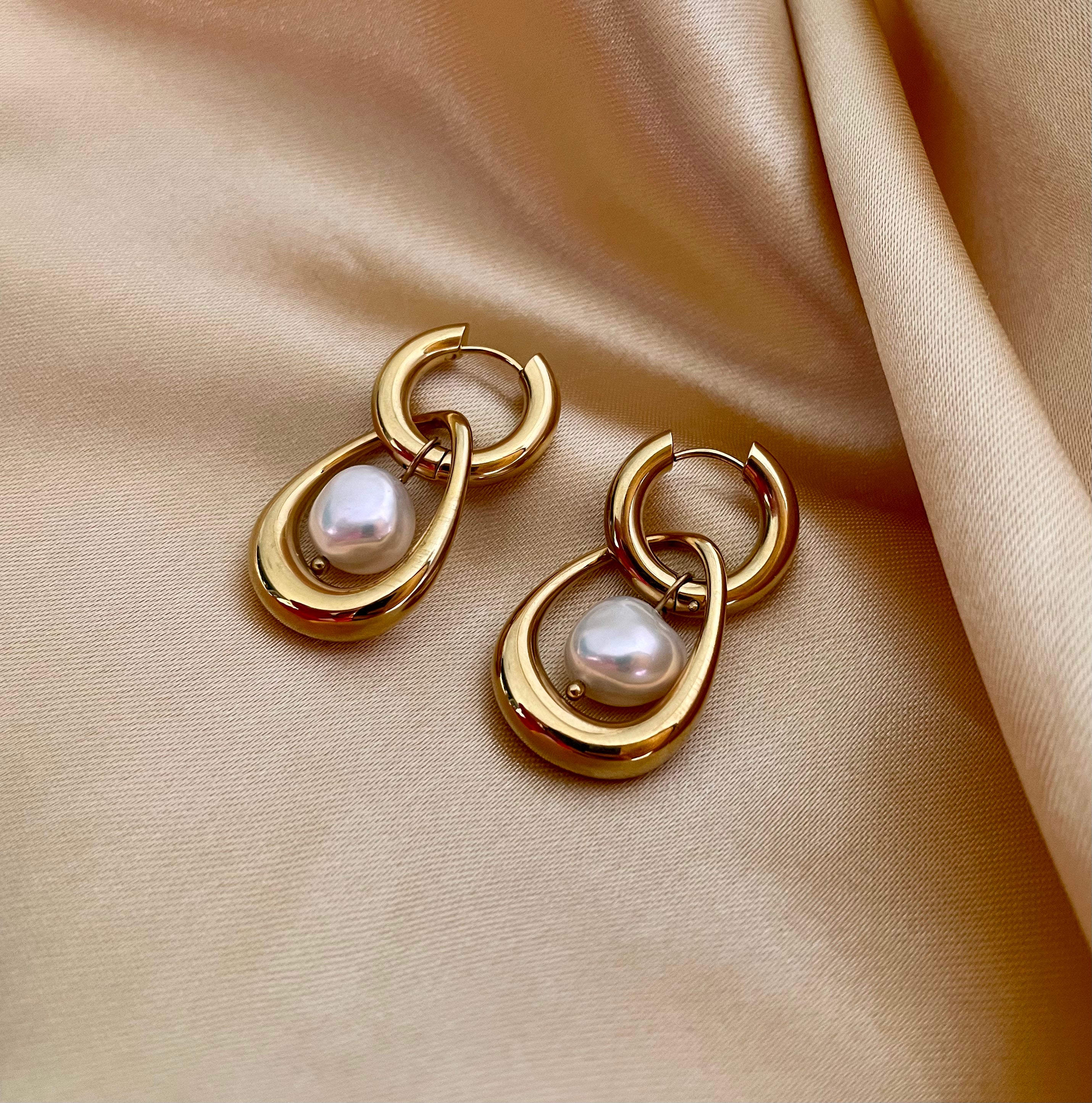 Close-up editorial photography of a gold hoop drop earring featuring a suspended organic white high-luster pearl. High-resolution luxury jewelry shot highlighting realistic gold texture and pearl iridescence.
