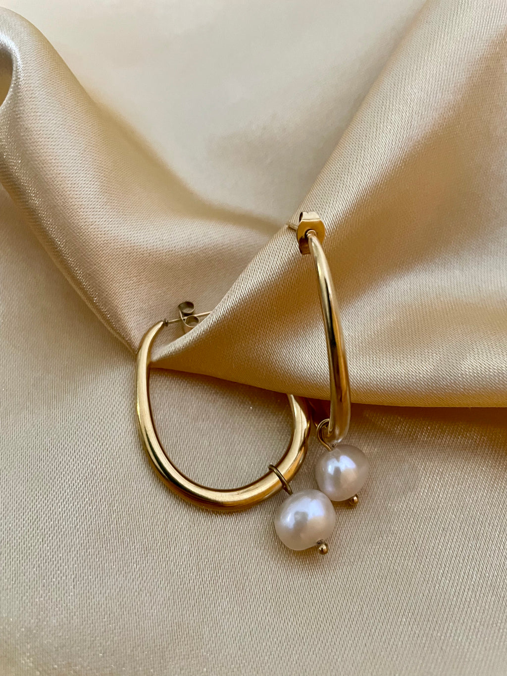 Close-up of a gold hoop earring with a single white pearl drop, highlighting the metallic luster and pearl detail against a soft neutral background