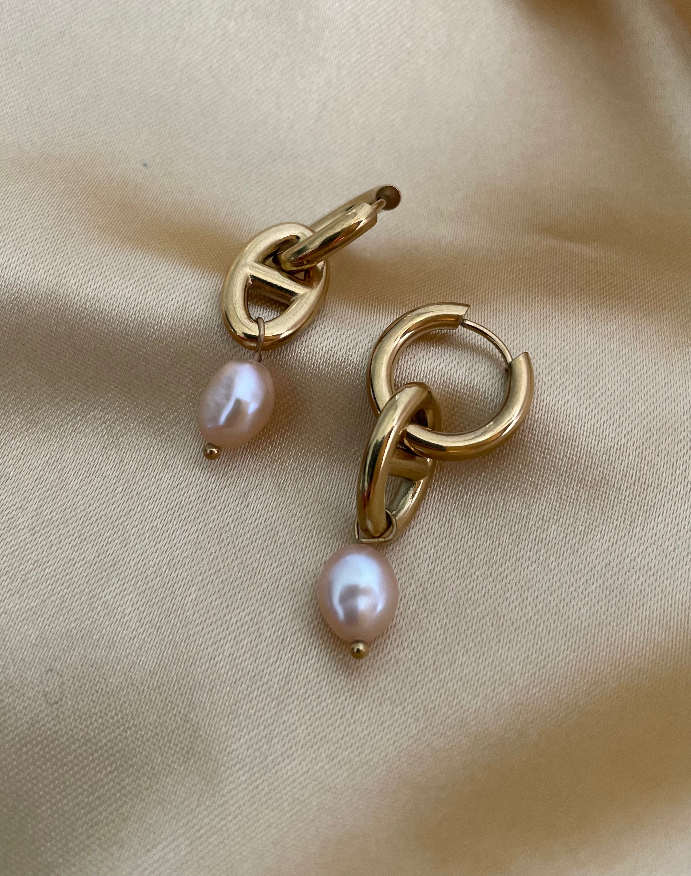 Gold hoop earrings with pearl drops on a beige fabric background