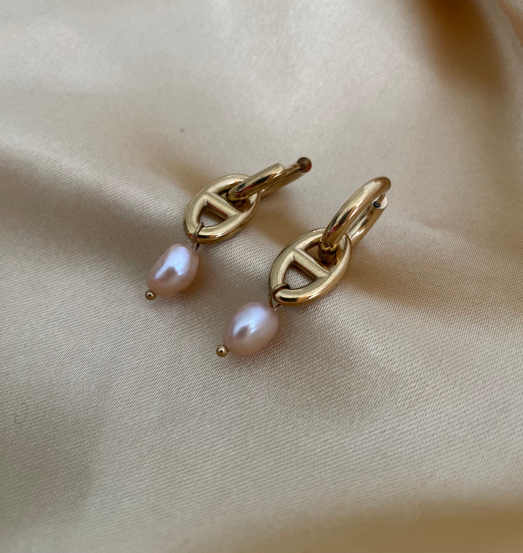 Gold earrings with pink pearls on a beige fabric background