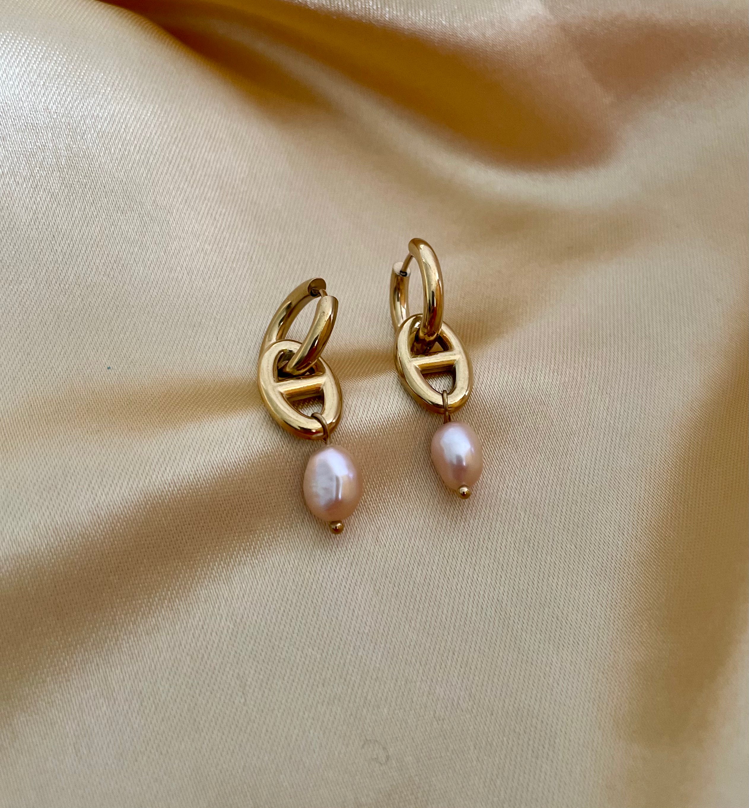 Gold hoop earrings with pearl drops on a beige fabric background