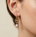 Gold hoop earring with a pink pearl on an ear against a neutral background