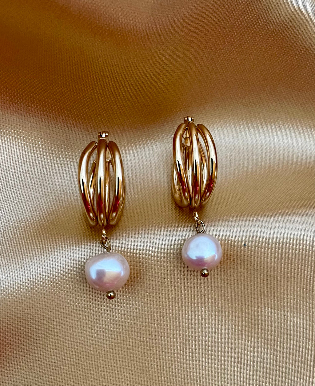 Luxury gold huggie earrings with white baroque pearl drop on model ear. High-luster freshwater pearl jewelry with triple-split gold hoop design in an editorial close-up