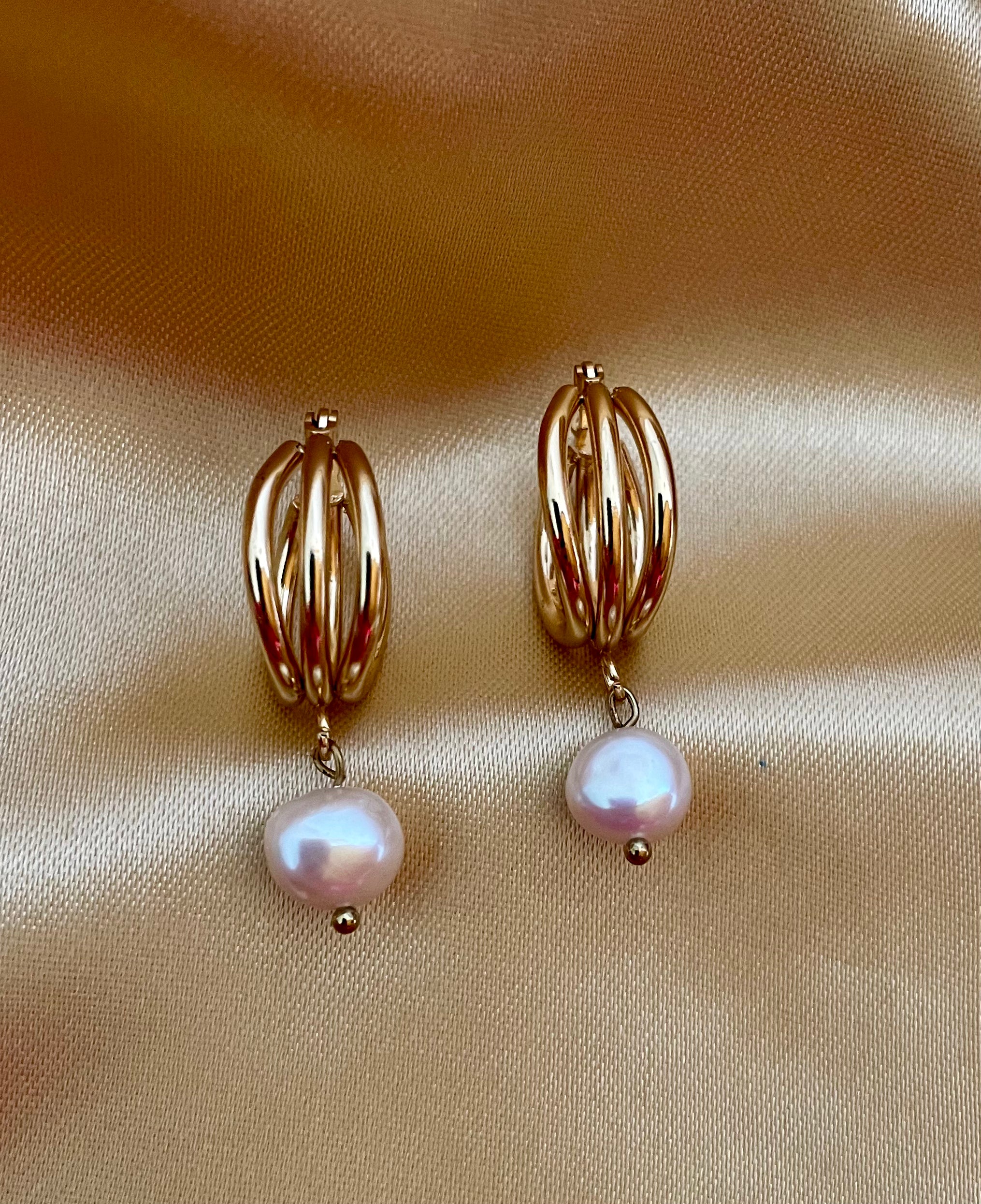 Luxury gold huggie earrings with white baroque pearl drop on model ear. High-luster freshwater pearl jewelry with triple-split gold hoop design in an editorial close-up