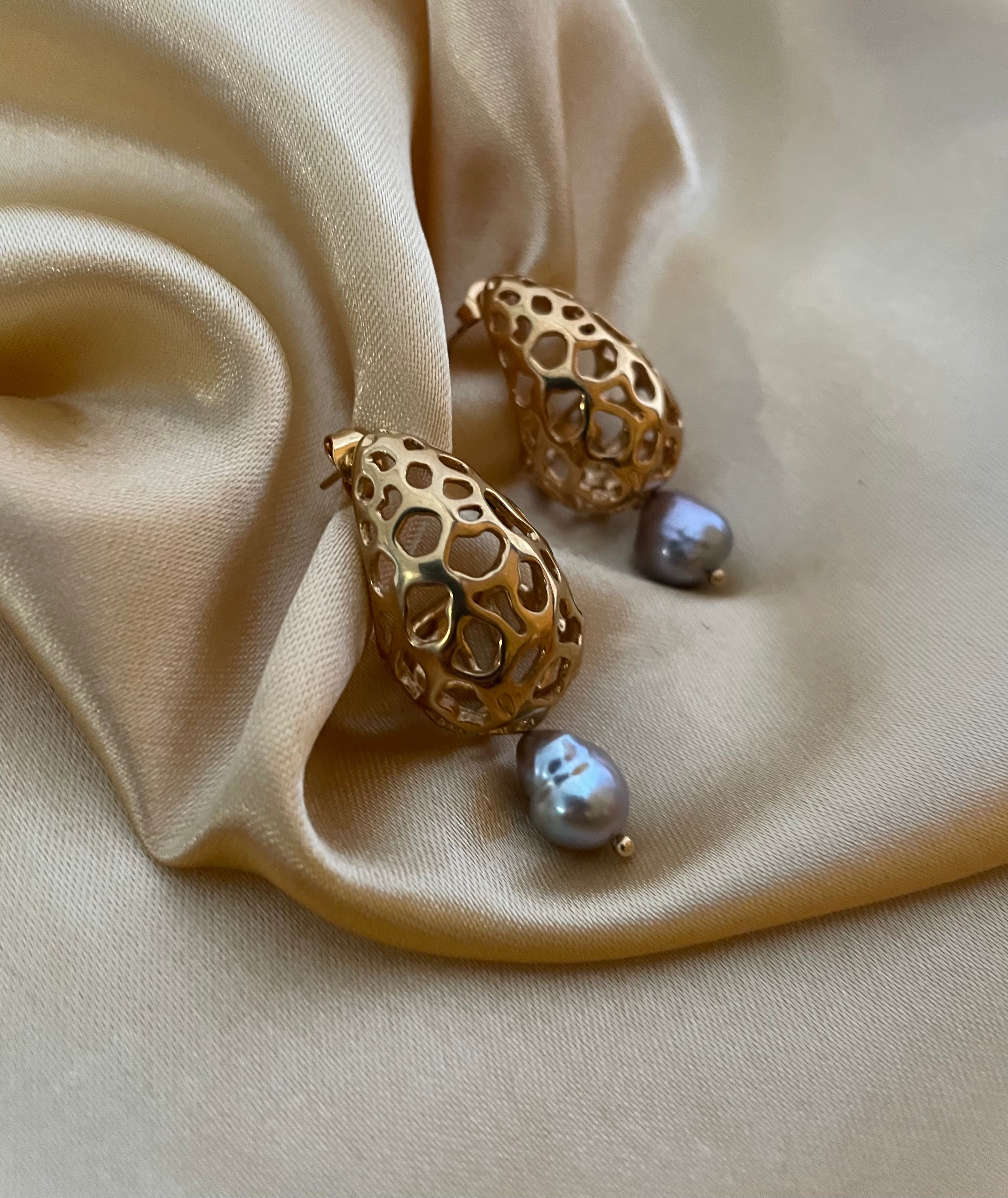 Close-up detail of luxury gold lattice teardrop earrings featuring a suspended metallic grey pearl with high chrome luster