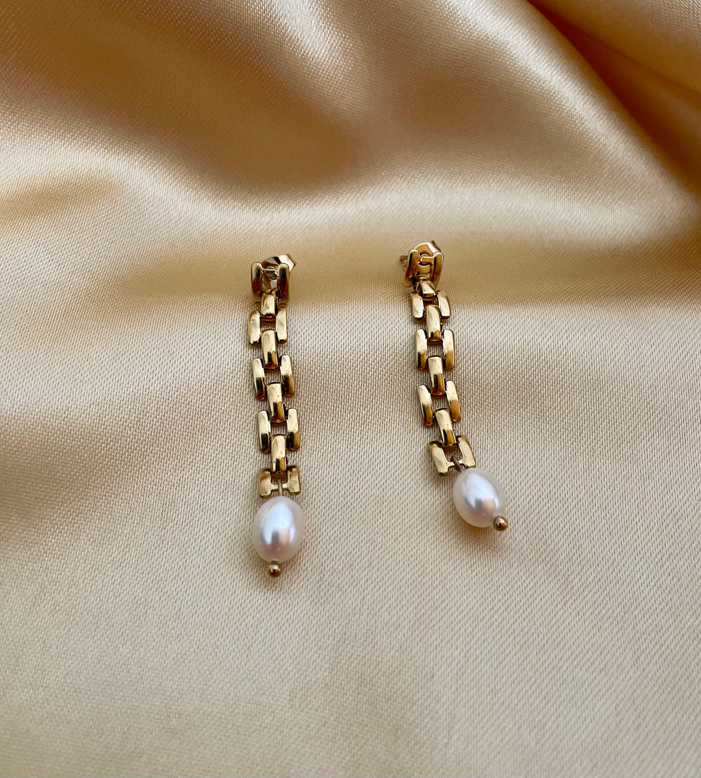 Gold rectangular link chain drop earrings featuring luminous white oval pearls on a beige silk background. Handcrafted Parisian pearl jewelry