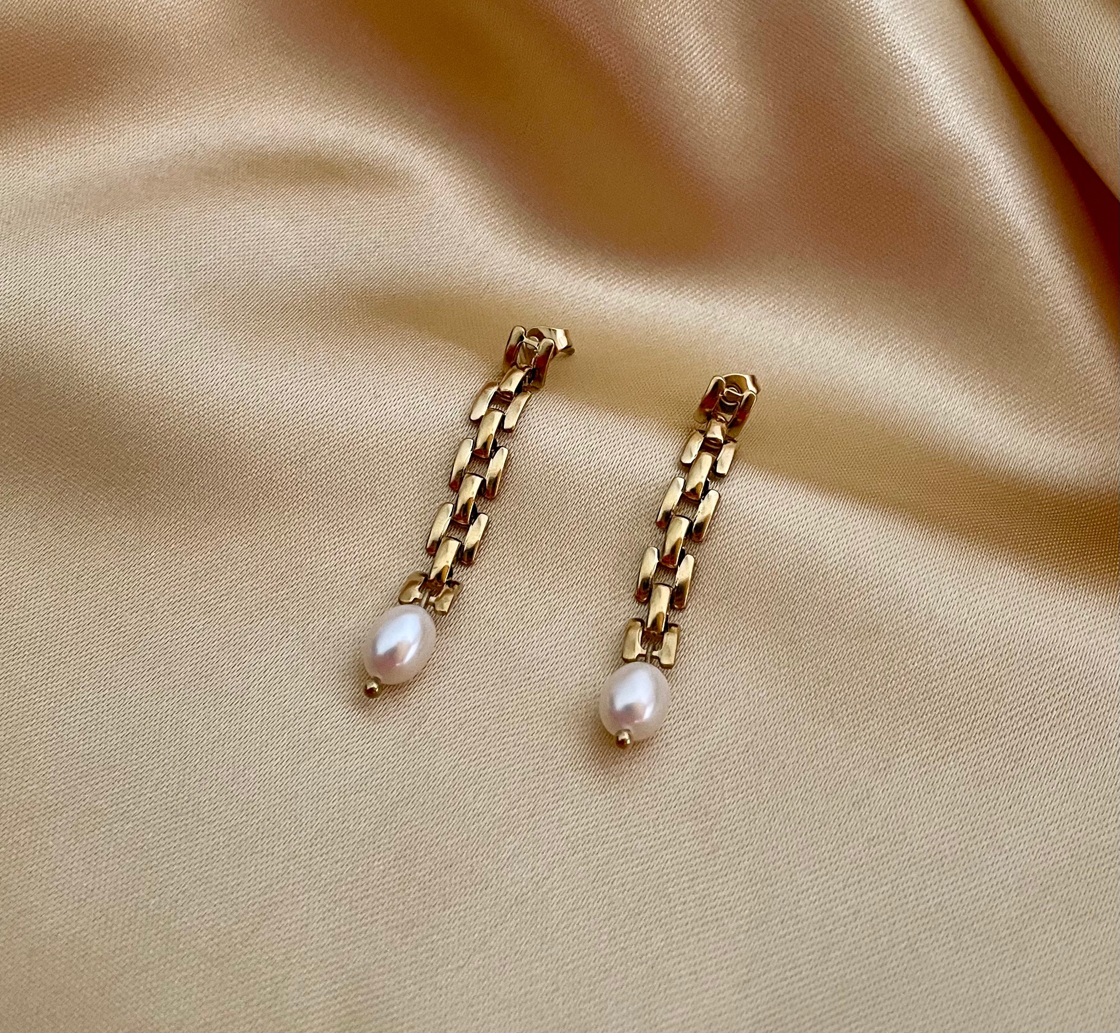 Gold rectangular link chain drop earrings featuring luminous white oval pearls on a beige silk background. Handcrafted Parisian pearl jewelry