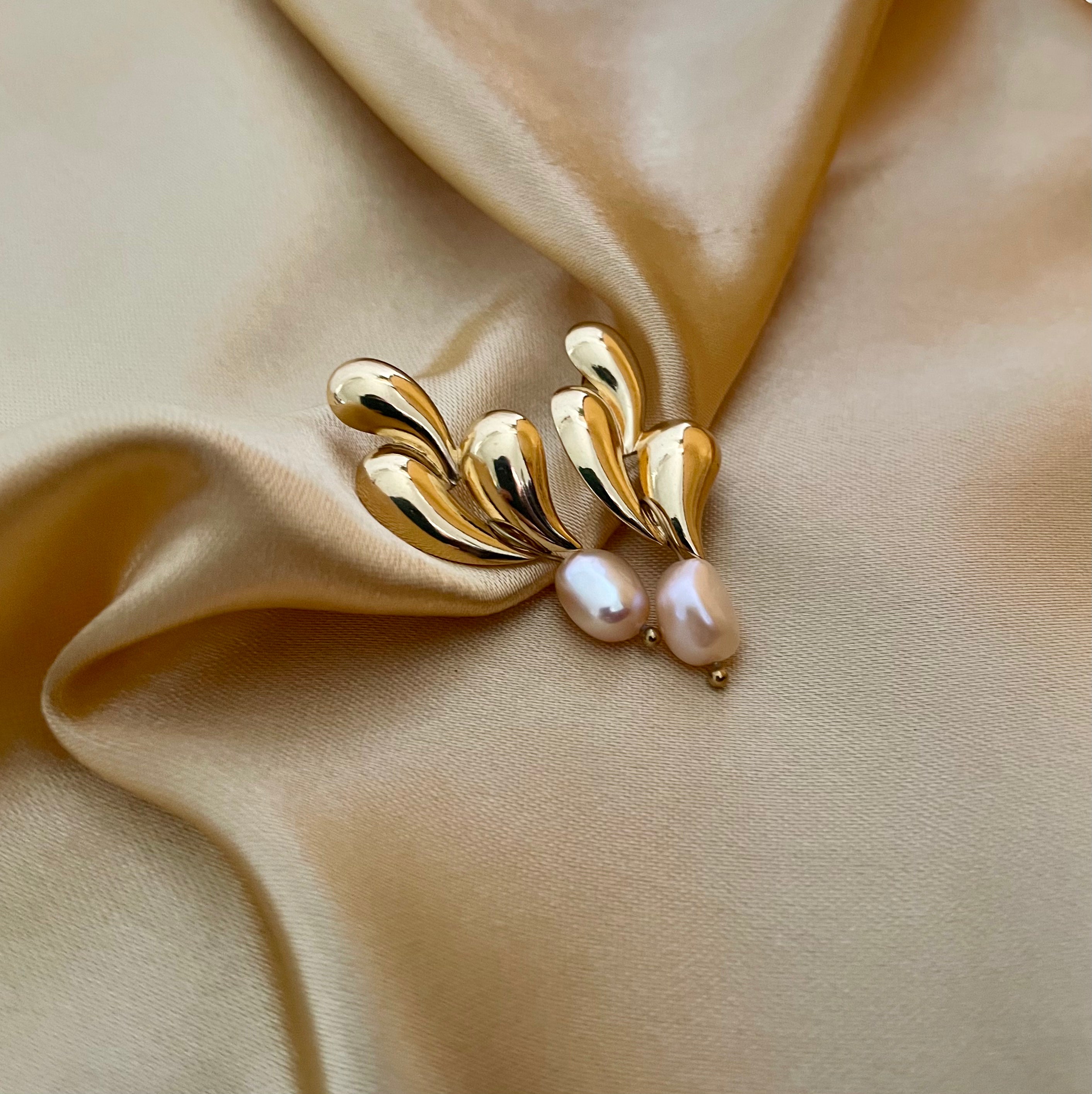 Editorial close-up of a unique, organic-shaped gold earrings featuring lustrous pink oval pearl drops