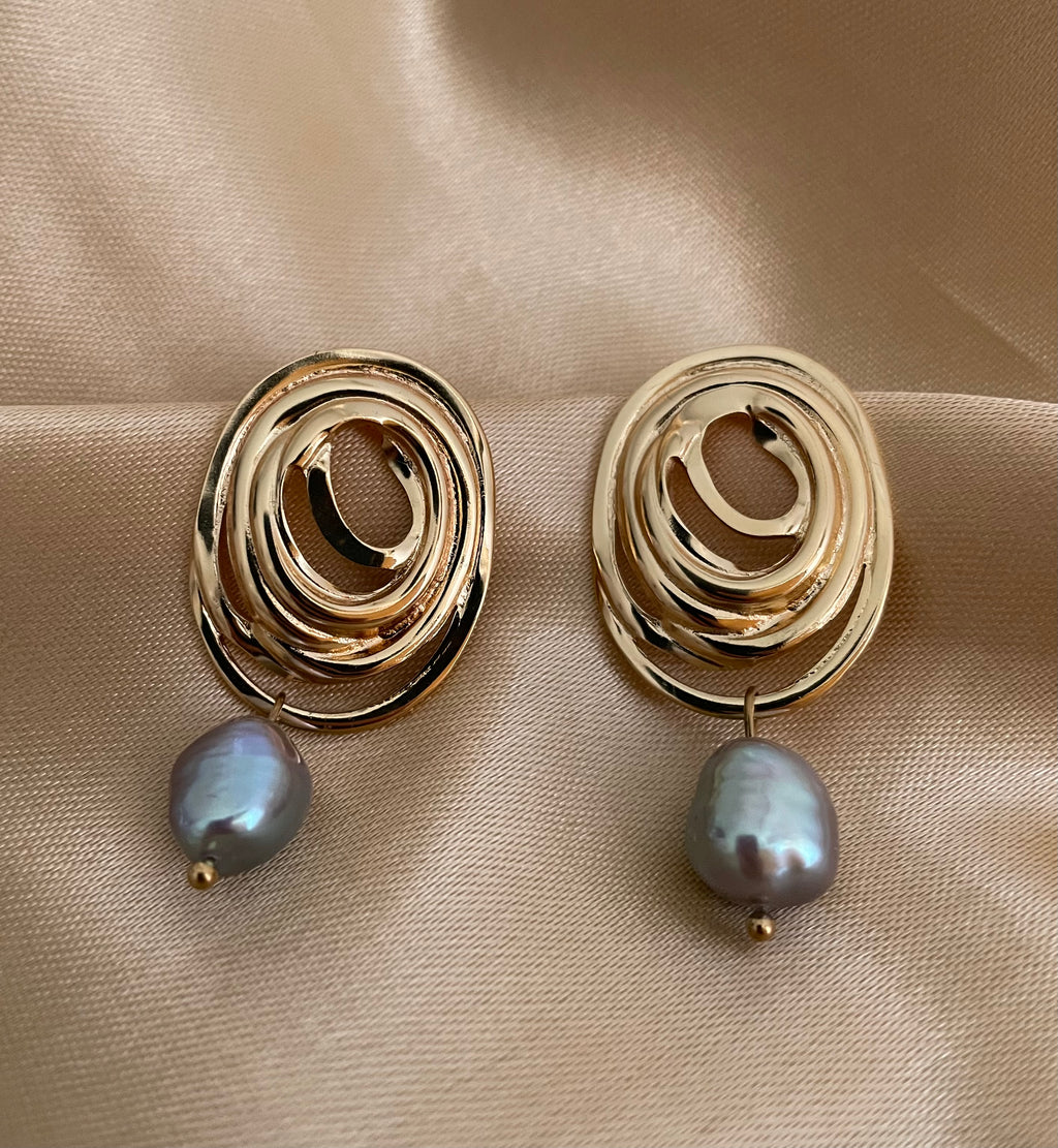 Close-up of a gold concentric spiral statement earrings with a lustrous organic freshwater grey pearl drop